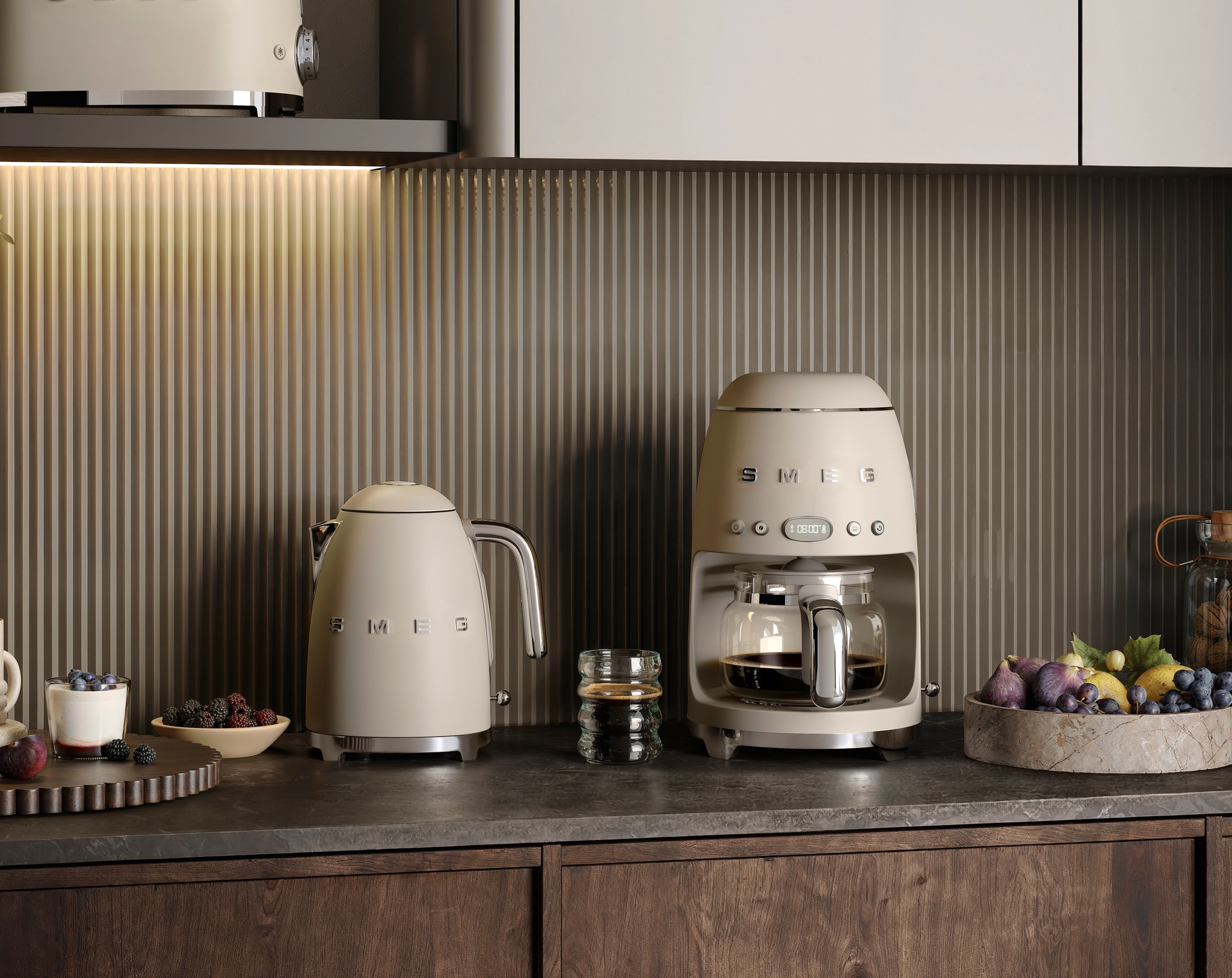 Stilrent kök med beige Smeg-kaffebryggare, vattenkokare och brödrost på en mörk bänkskiva.