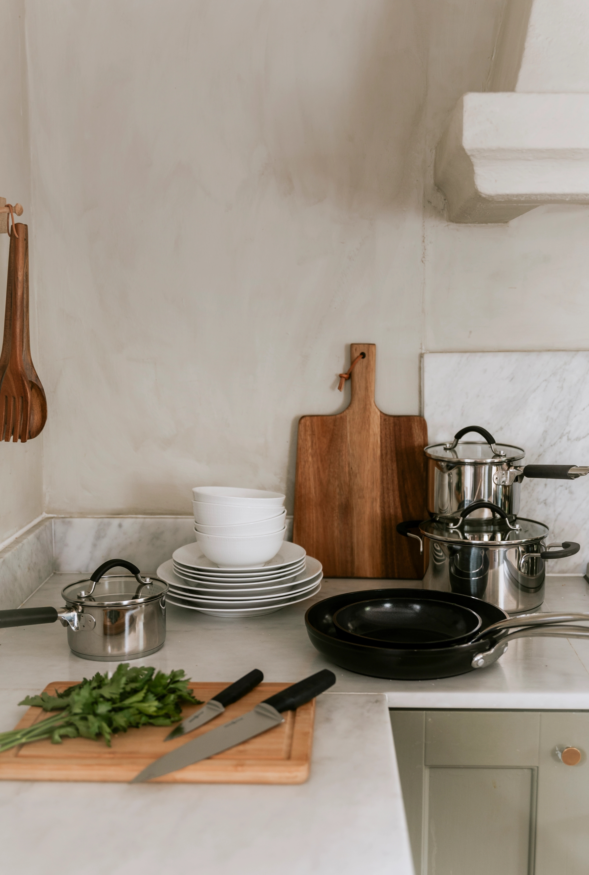En kjøkkenbenk med kjeler og panner, tallerkener, kniver og en skjærefjøl