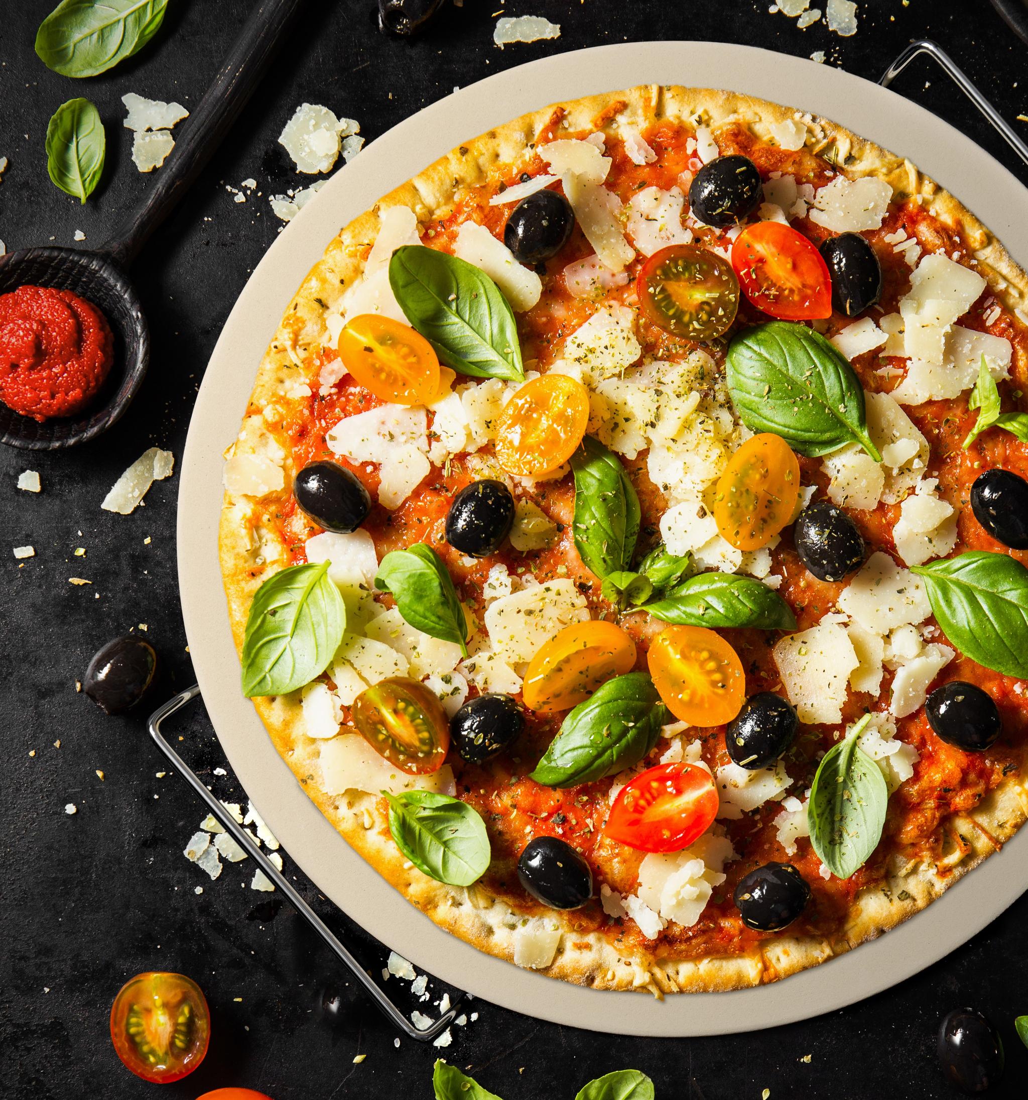a pizza with tomatoes , olives , basil and cheese on a plate .