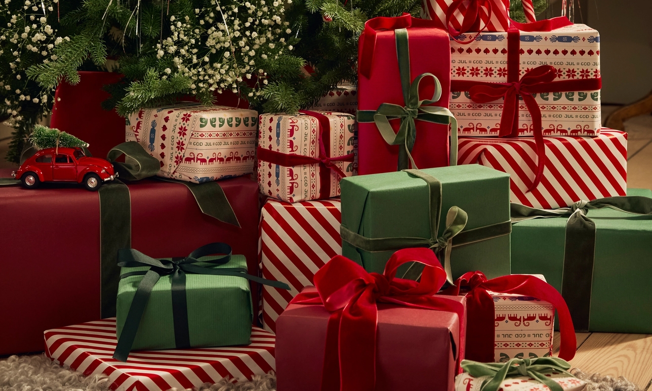 Juhlava kasa punaisia, vihreitä ja kuviollisia joululahjoja kuusen alla, pienen punaisen auton kanssa.