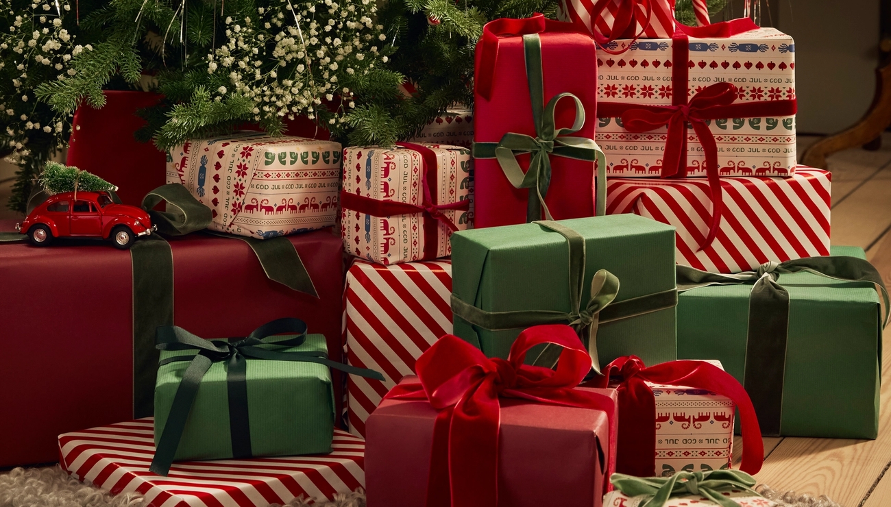 Juhlava kasa punaisia, vihreitä ja kuviollisia joululahjoja kuusen alla, pienen punaisen auton kanssa.