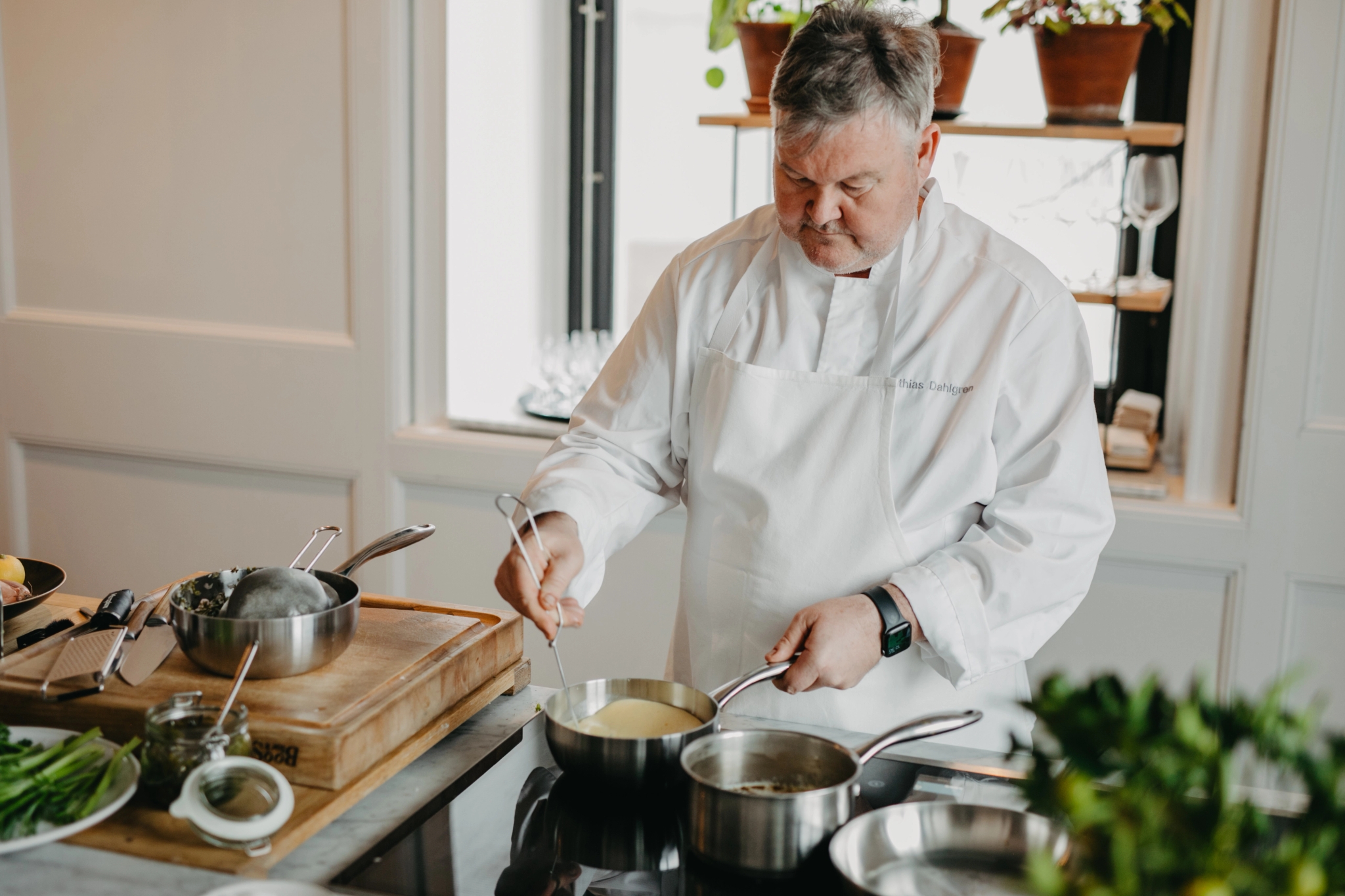 En kock i vit rock rör om i en kastrull på spisen.