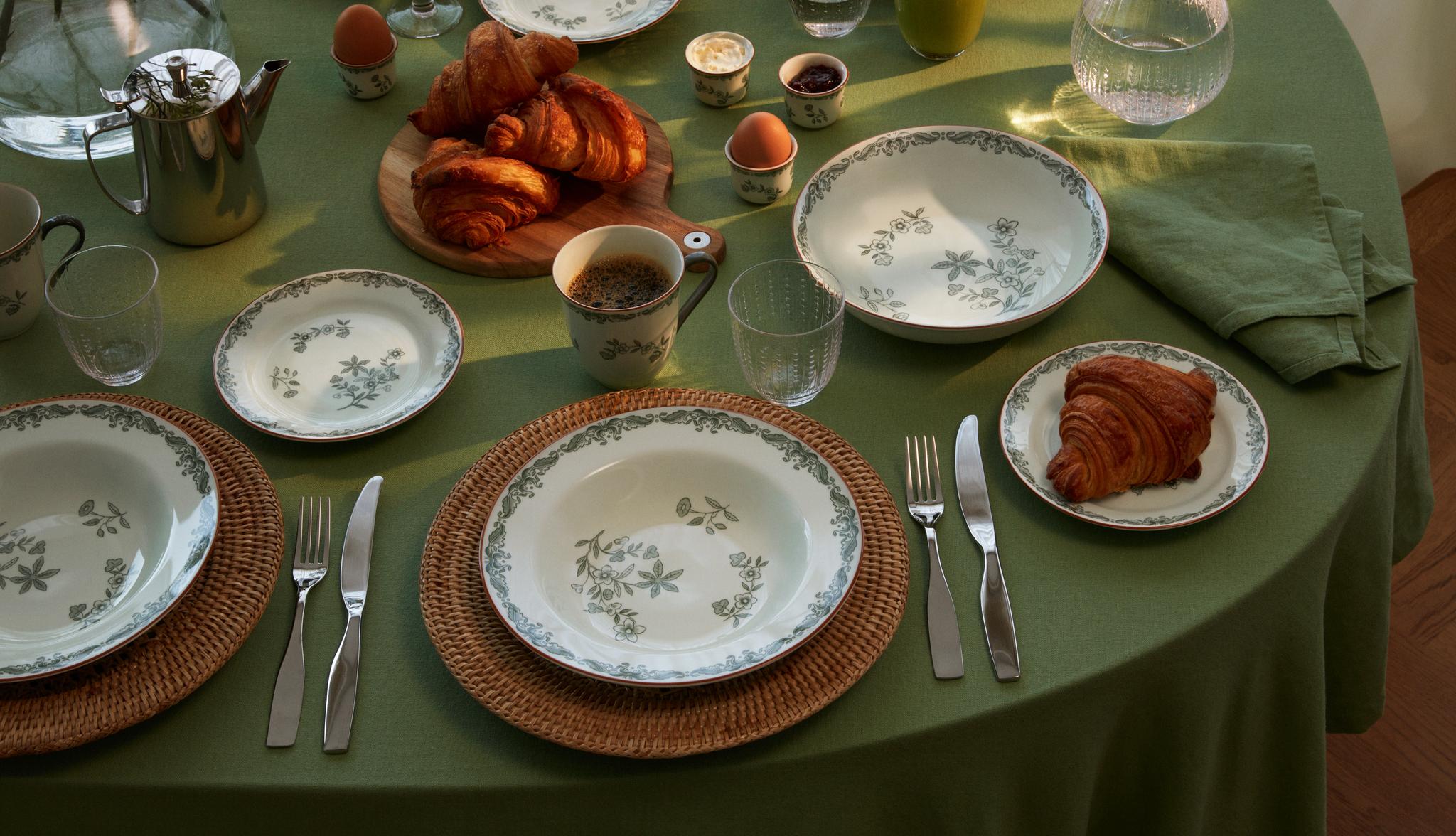 Frokostbord med grønn duk, blomstrete servise, croissanter, egg, kaffe og juice.