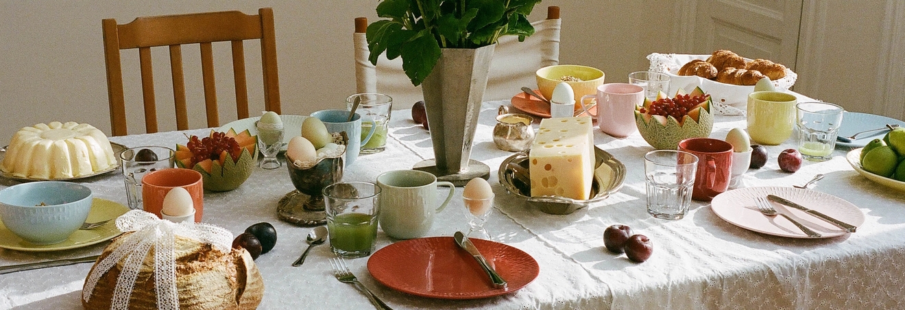 Vackert dukat frukostbord med solrosor, nybakat bröd, ost, frukt och färgglada tallrikar i morgonljus.