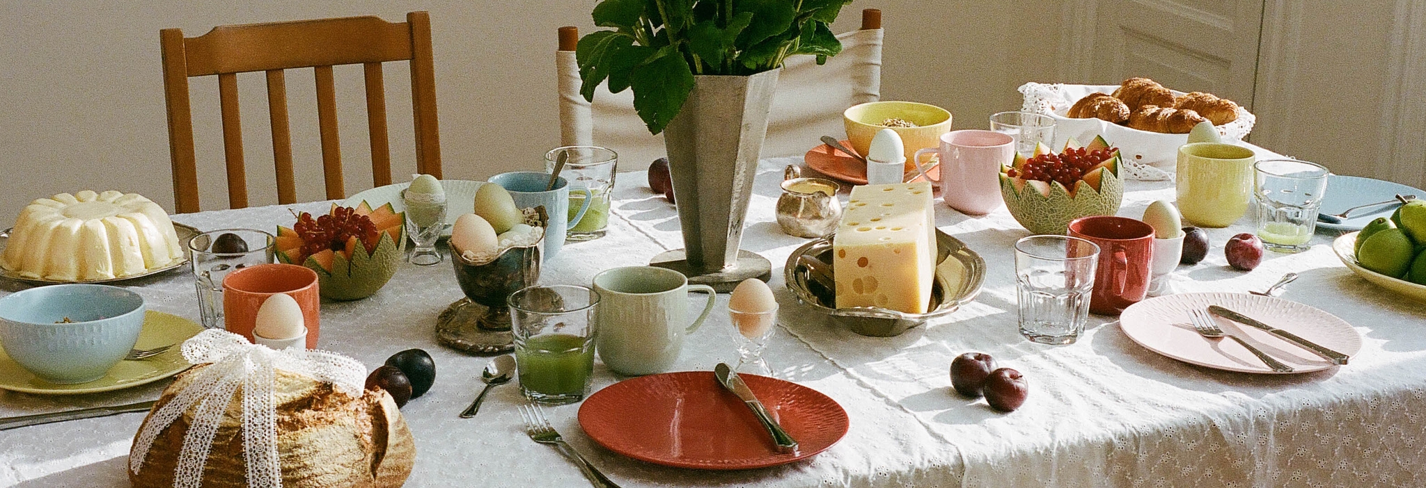 Vackert dukat frukostbord med solrosor, nybakat bröd, ost, frukt och färgglada tallrikar i morgonljus.