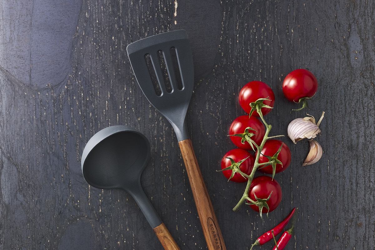 Köksredskap från Scanpan på ett svart bord med tomater och vitlök bredvid