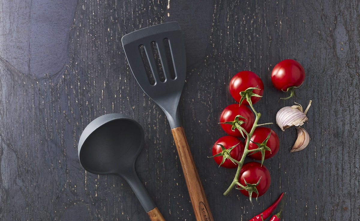 Köksredskap från Scanpan på ett svart bord med tomater och vitlök bredvid