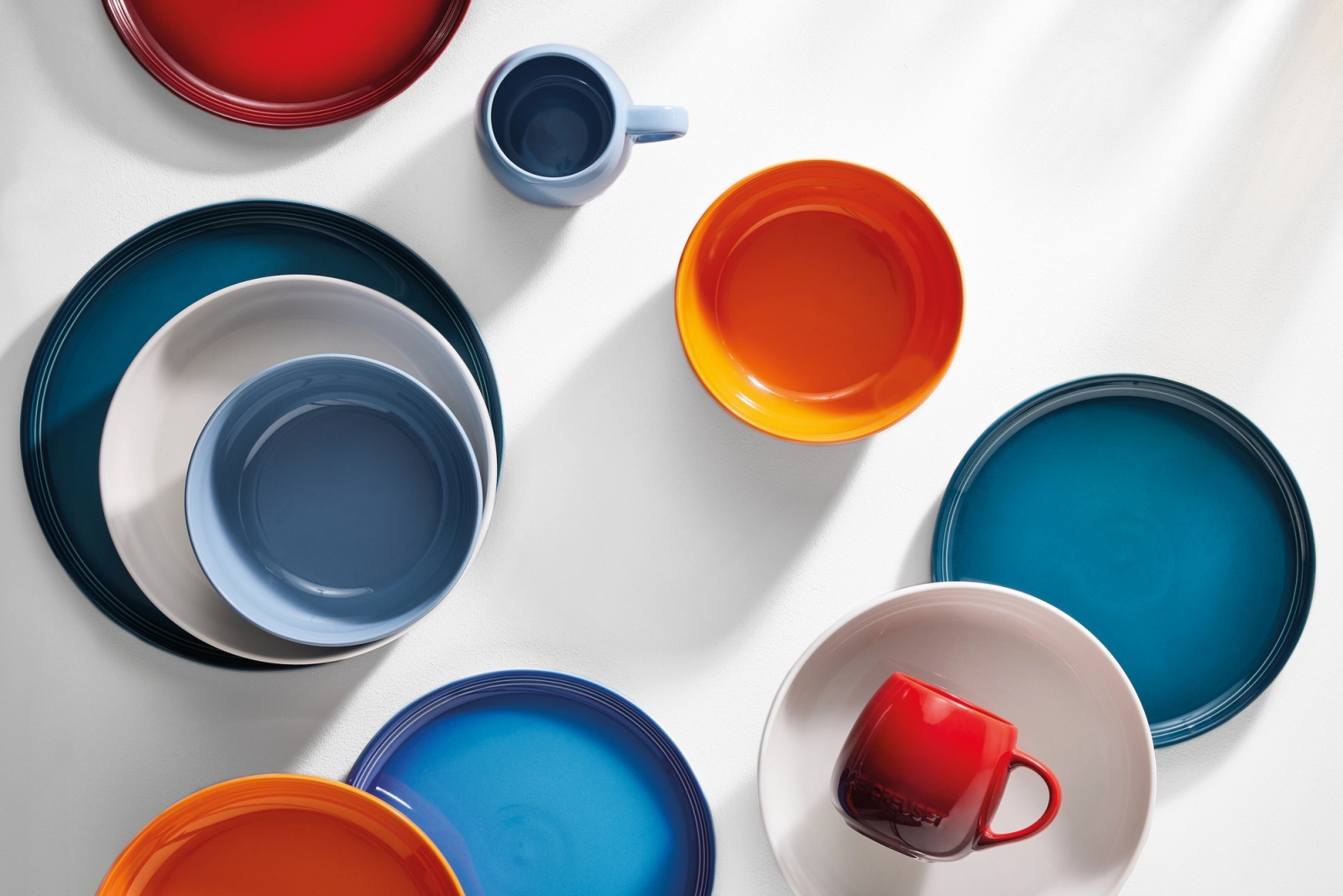 Le Creuset tallrikar i blått, orange, vitt och rött på ett ljust bort