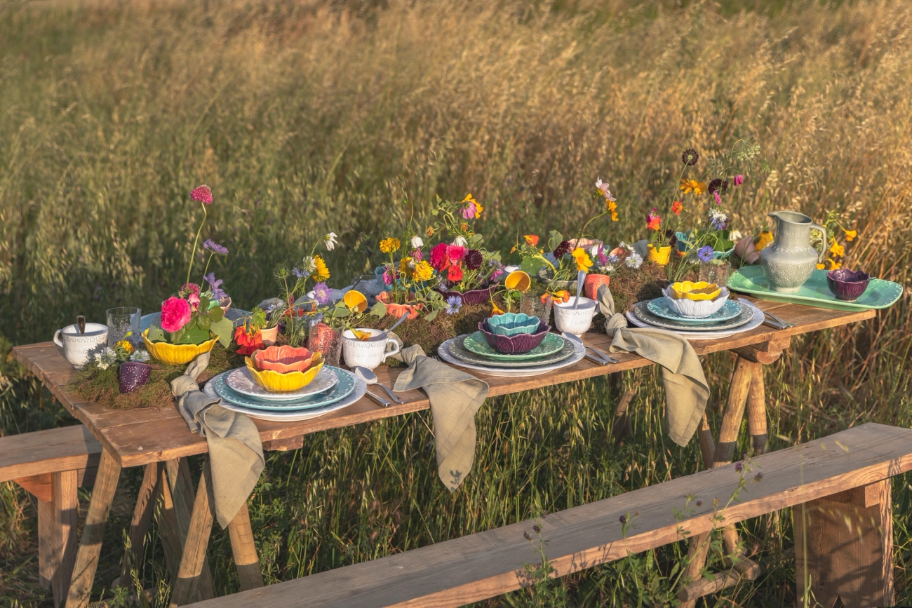 Festlig borddekking med hvit duk, dekkebrikker, hvitt porselen og gule og blå vaser med blomster i