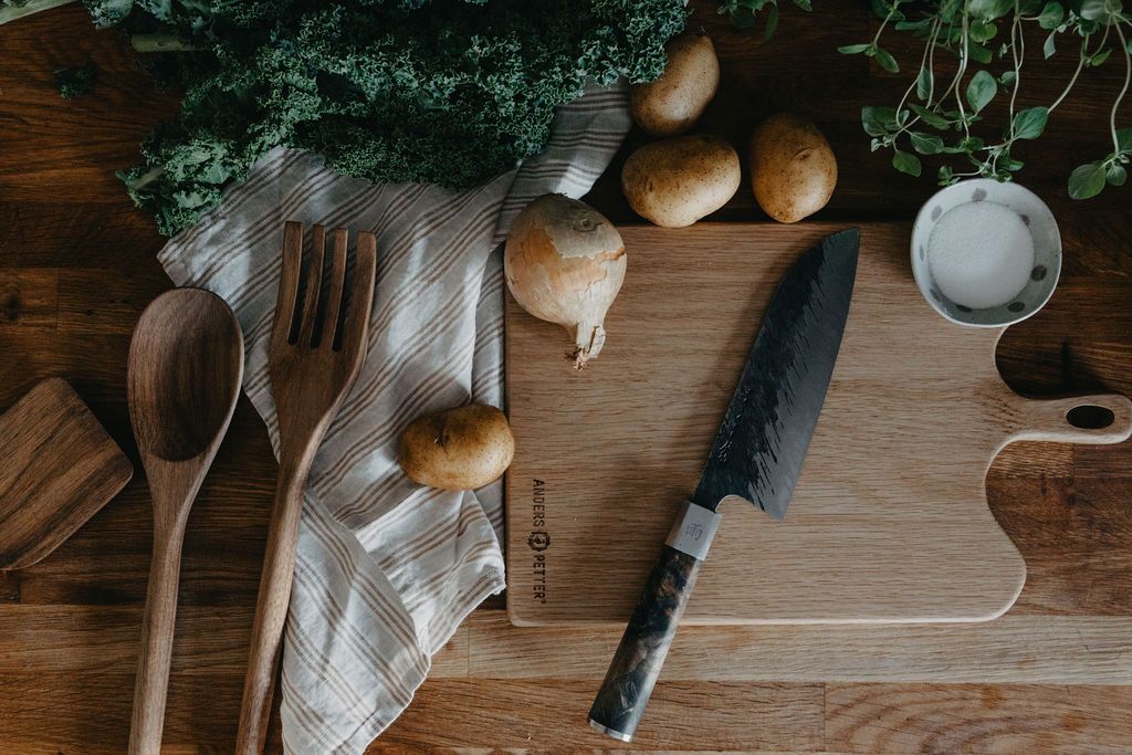Färska grönsaker, köksredskap i trä och en kniv arrangerade på ett träbord