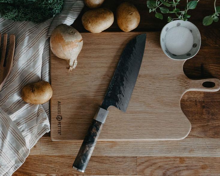 Färska grönsaker, köksredskap i trä och en kniv arrangerade på ett träbord