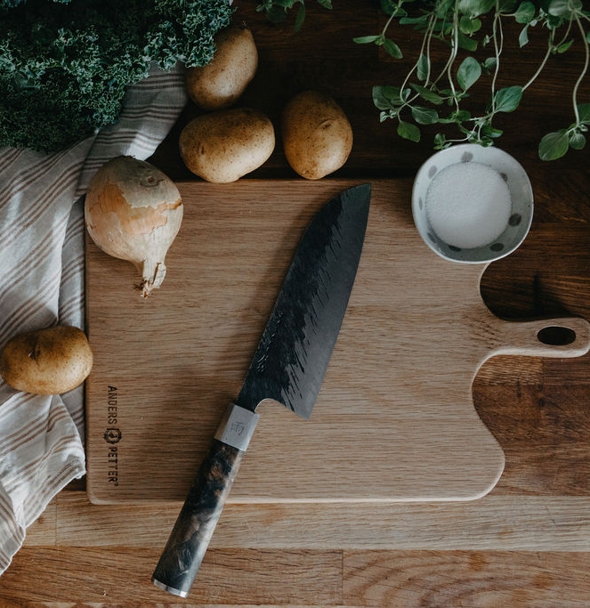 Färska grönsaker, köksredskap i trä och en kniv arrangerade på ett träbord