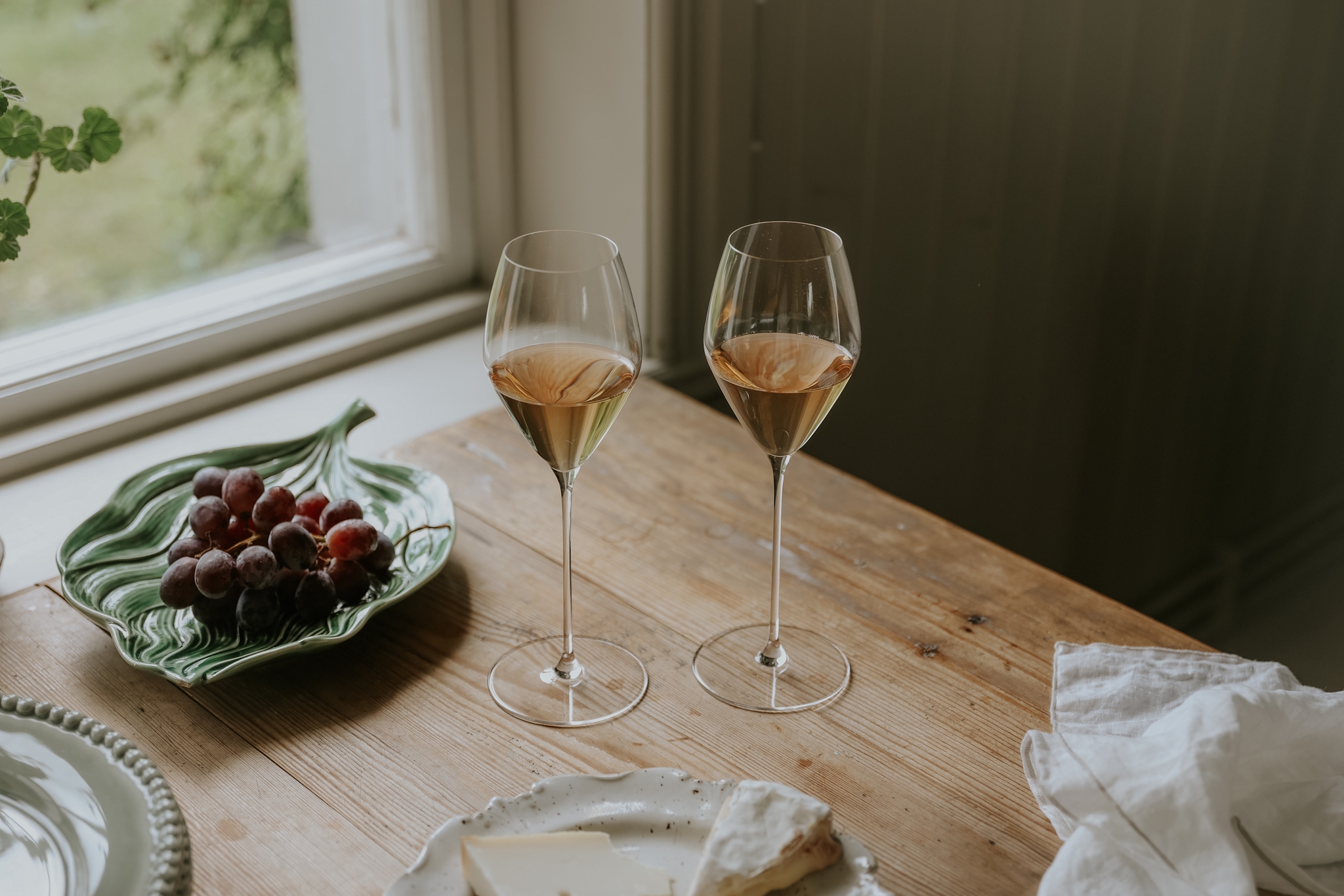 Matplats med fokus på två vinglas och ett serveringsfat med vindruvor på som står på ett ljust träbord