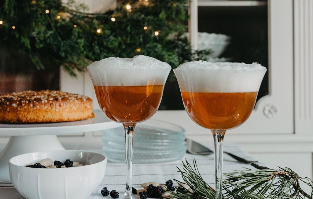 Två glas Saffransglögg Sour med skum, bredvid en julkrans och en saffranskrans på ett dukat bord