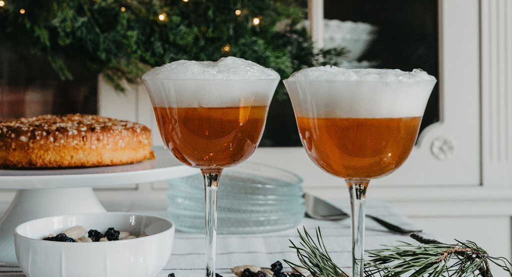 Två glas Saffransglögg Sour med skum, bredvid en julkrans och en saffranskrans på ett dukat bord