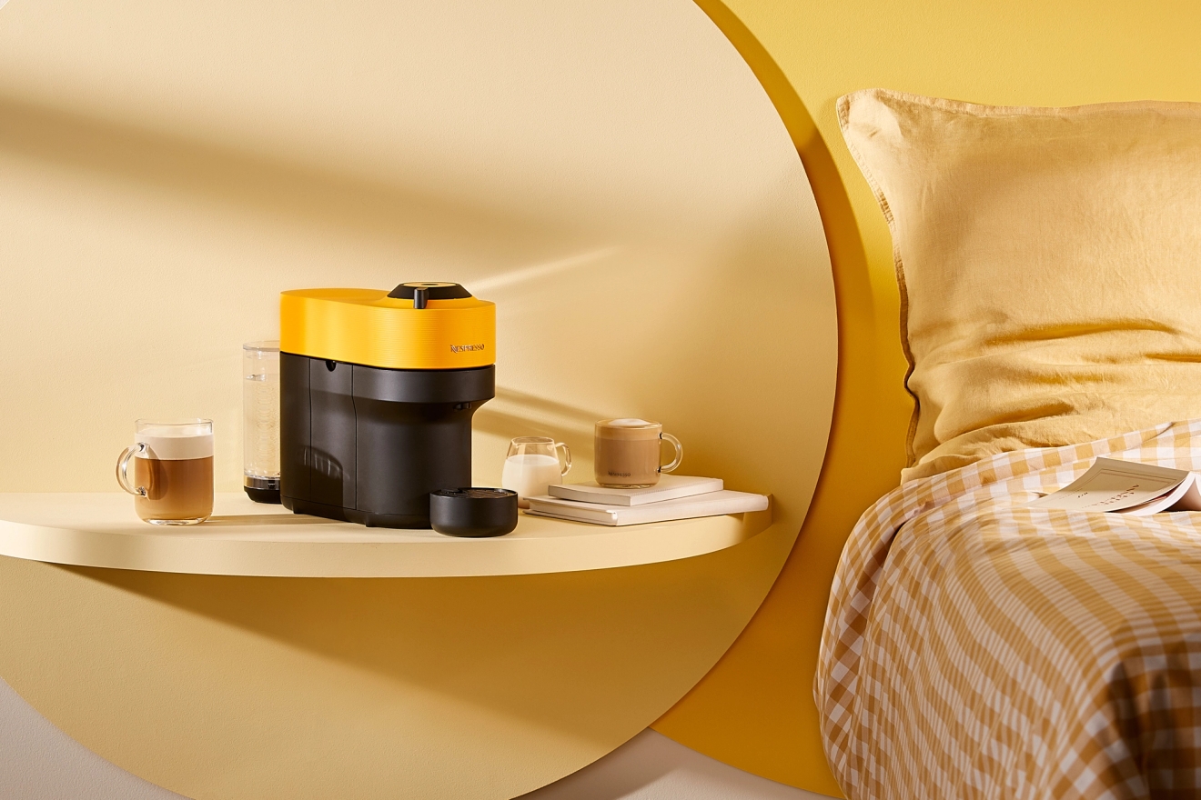musta/keltainen kapselikeitin pöydällä sängyn vieressä keltaisessa huoneessa