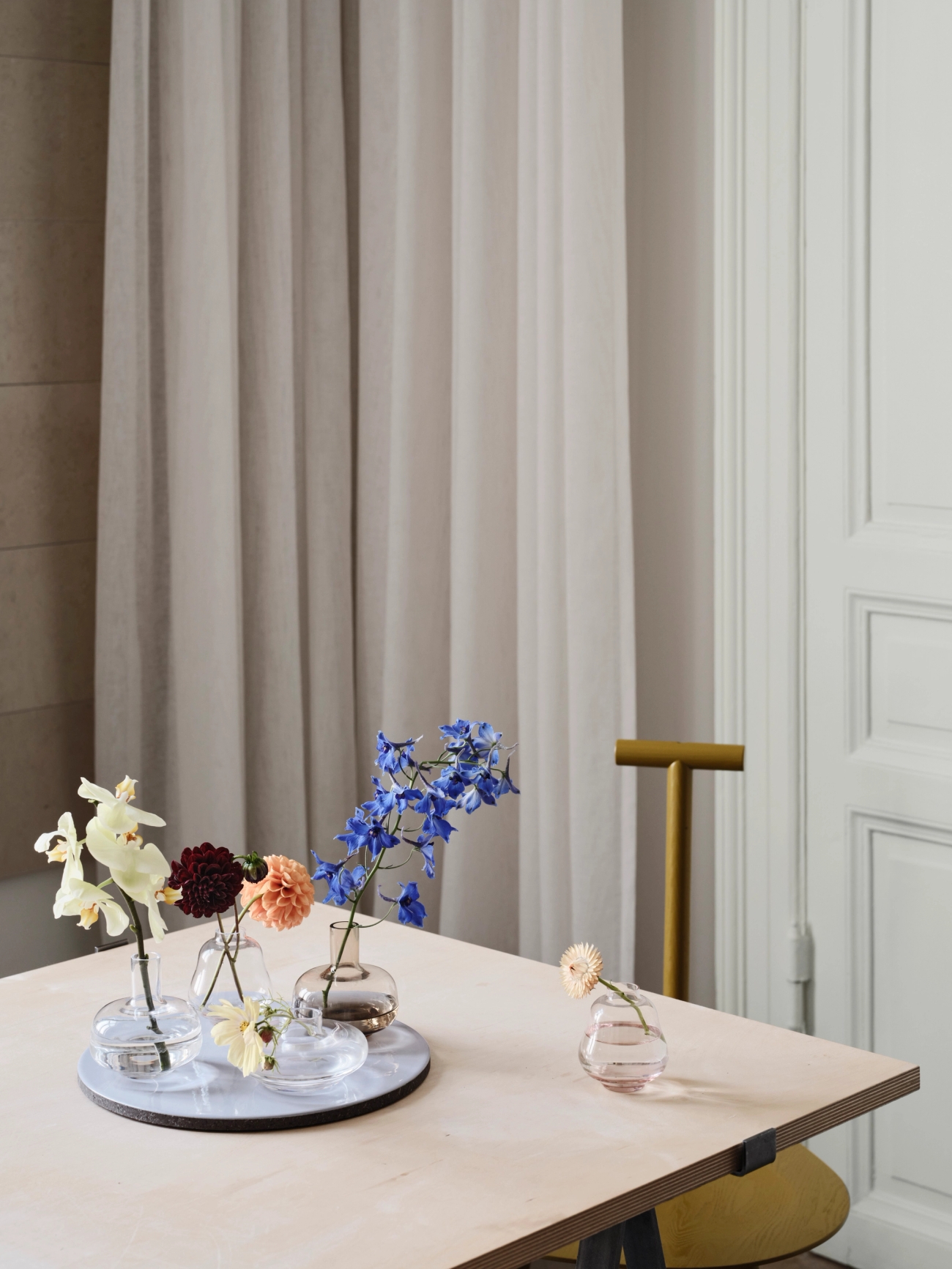 Ulike blomster i glassvaser og på et hvitt brett, plassert på et trebord.