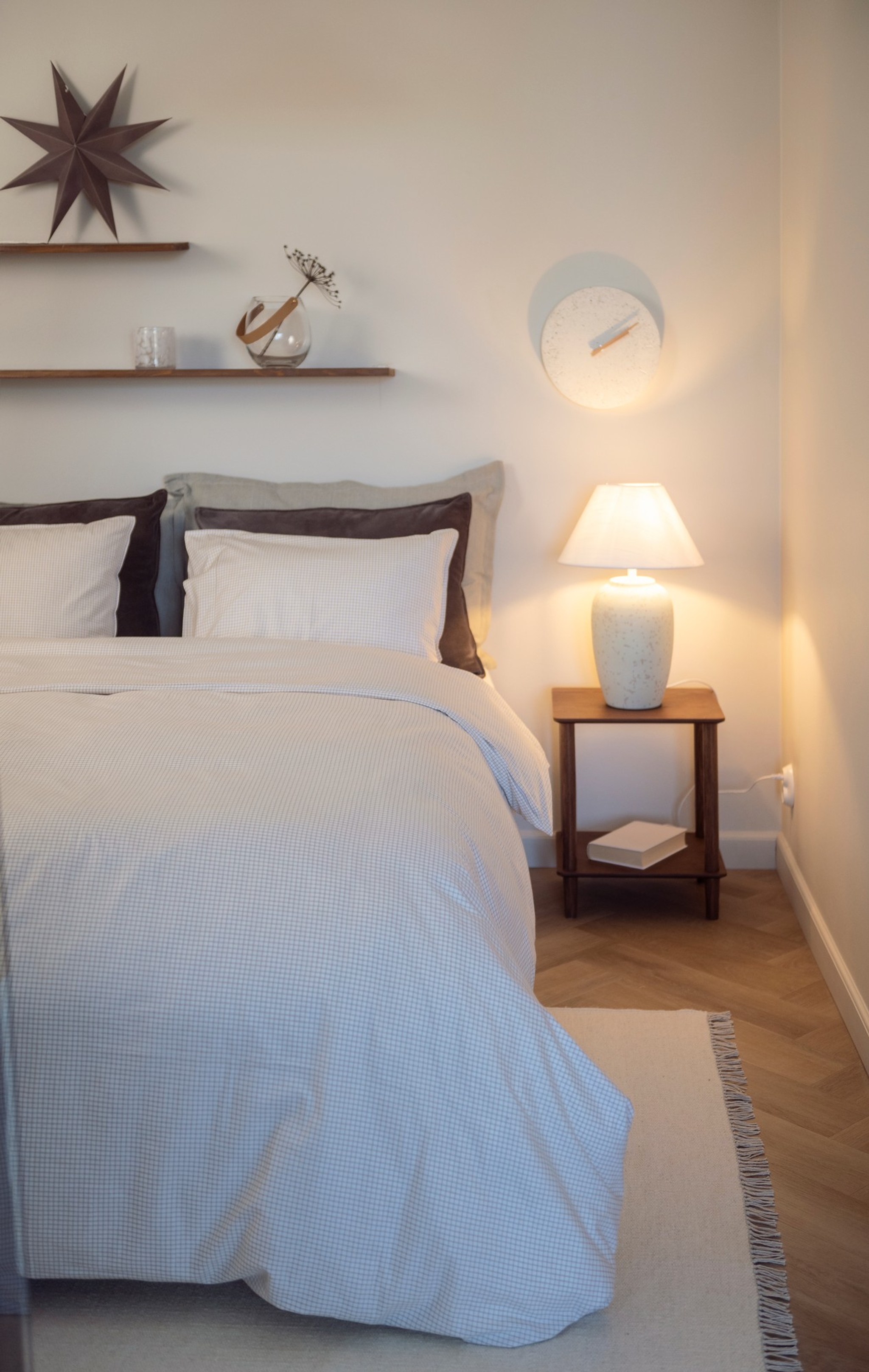 Sovrum med Fanni K inredning med en stor vit bäddad dubbelsäng, beige matta och ett träbord med en lampa på