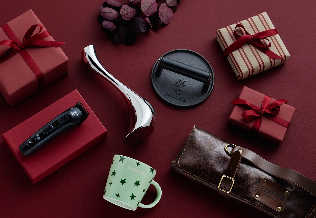 Olika presenter inklusive en trimmer, en mugg och inslagna presentaskar arrangerade på en röd yta.