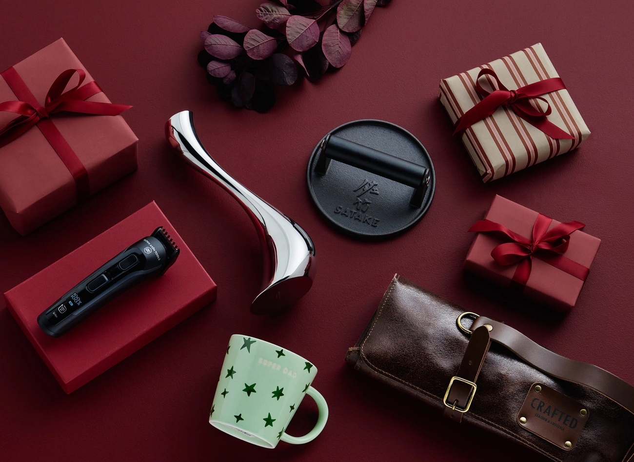 Olika presenter inklusive en trimmer, en mugg och inslagna presentaskar arrangerade på en röd yta.