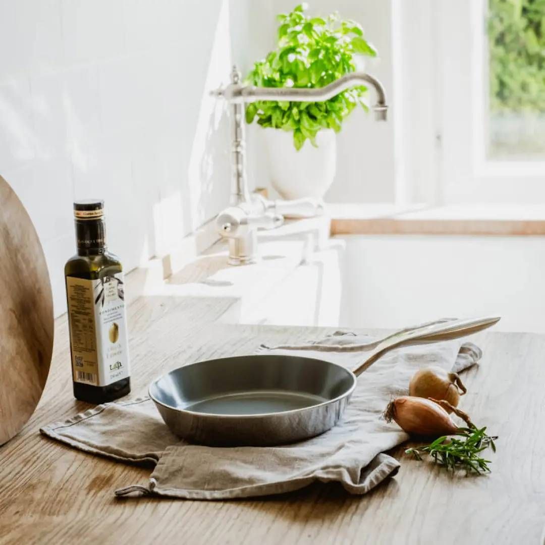 Heirol cerasafe paistinpannu, oliiviöljyä ja tuoreita raaka-aineita keittiötasolla.
