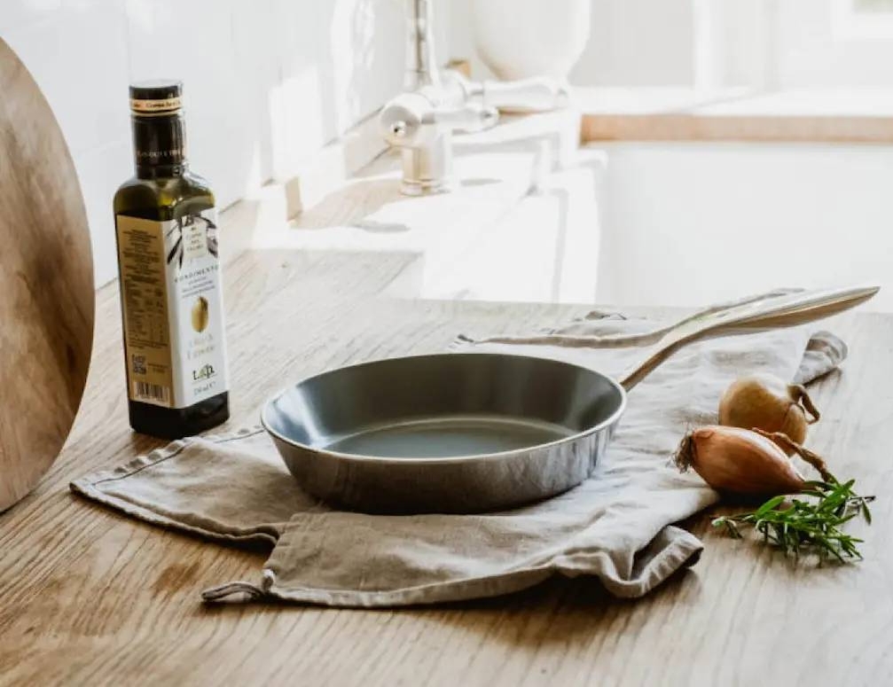 Heirol cerasafe paistinpannu, oliiviöljyä ja tuoreita raaka-aineita keittiötasolla.