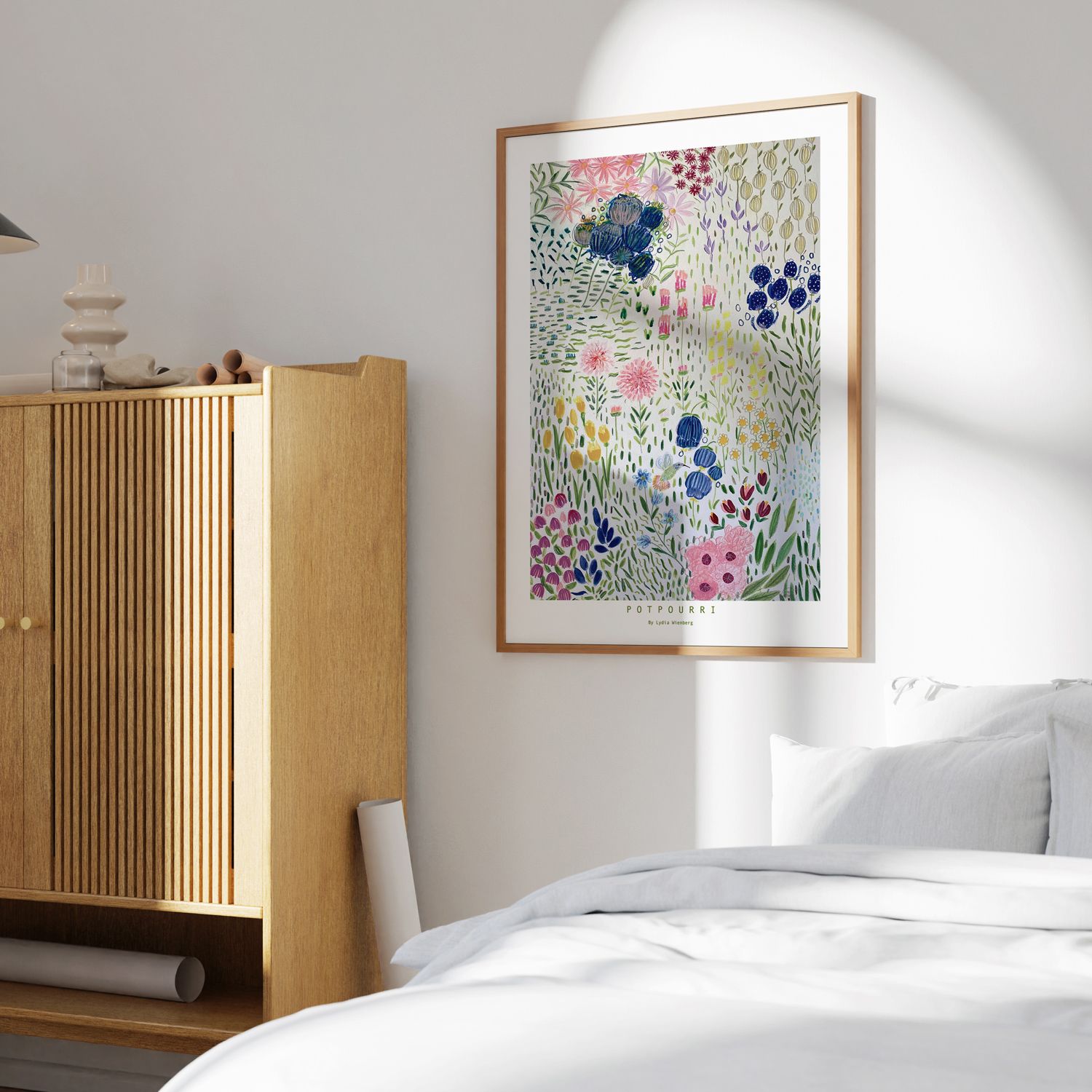 Ett inramat tryck av färgglada vildblommor hänger på en vit vägg i ett ljust sovrum.