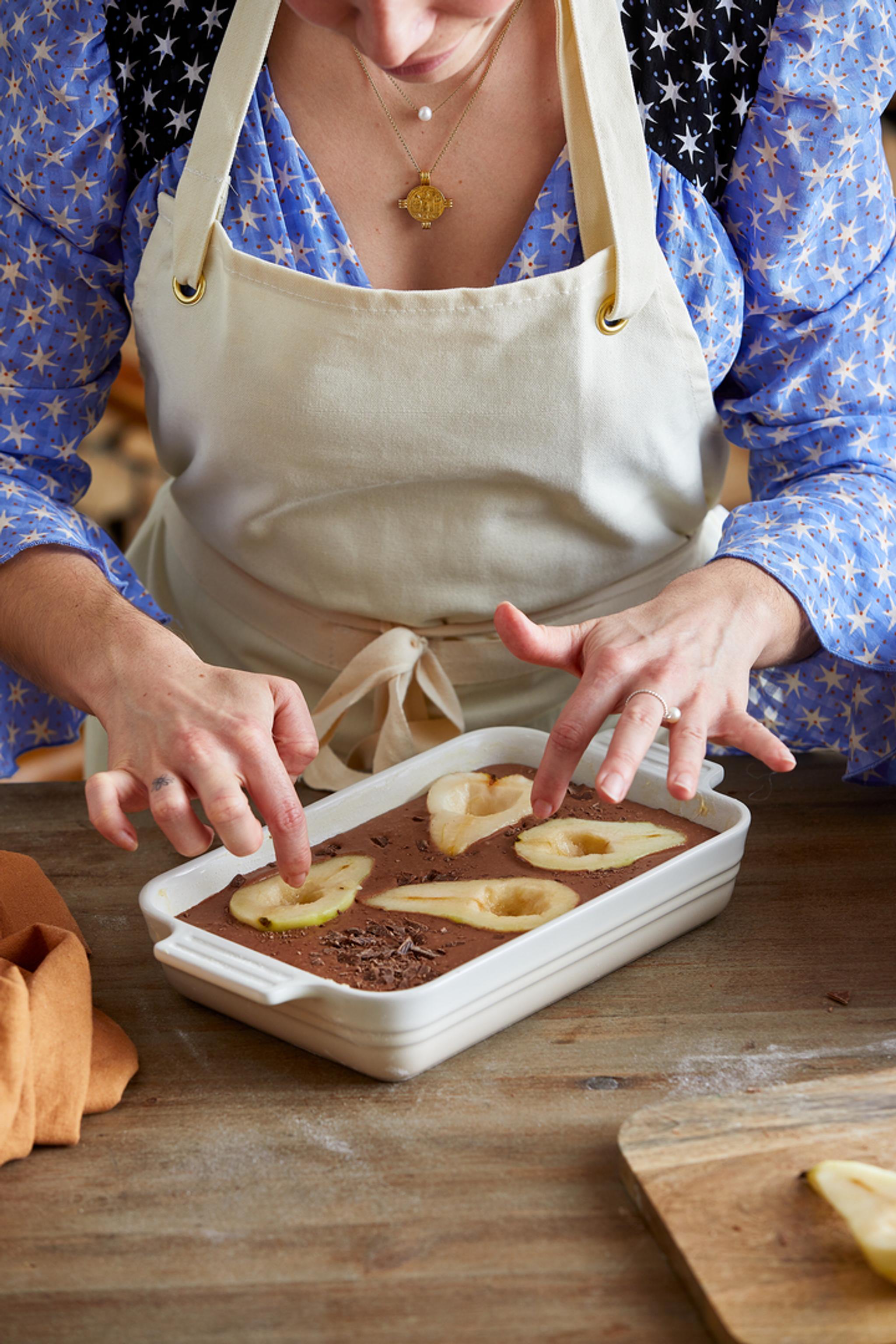 En kvinne med forkle forbereder en dessert med sjokolade og pærer.