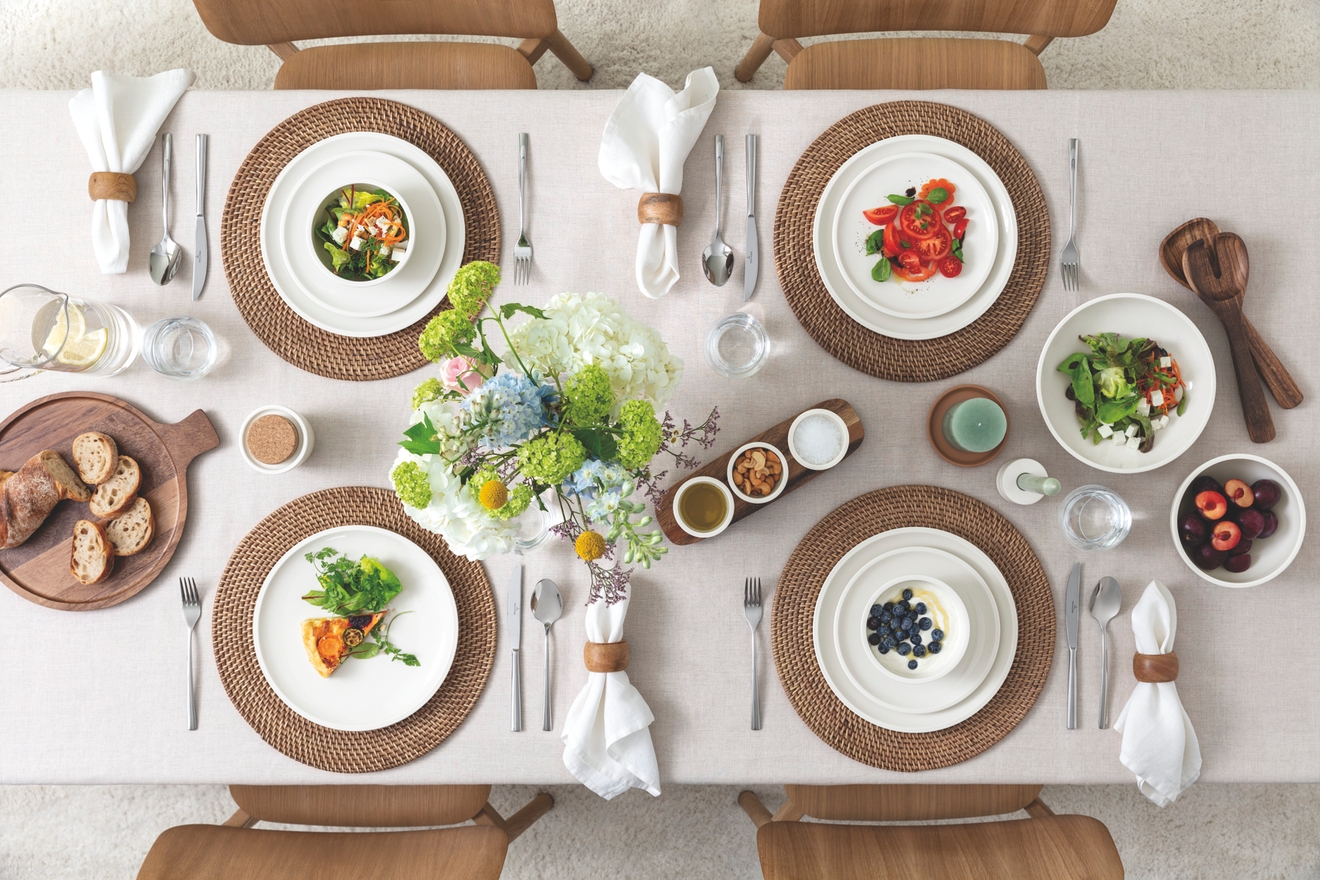 Vackert dukat matbord uppifrån med somrig sallad, frukt, bröd och blommor i ljus, skandinavisk stil.