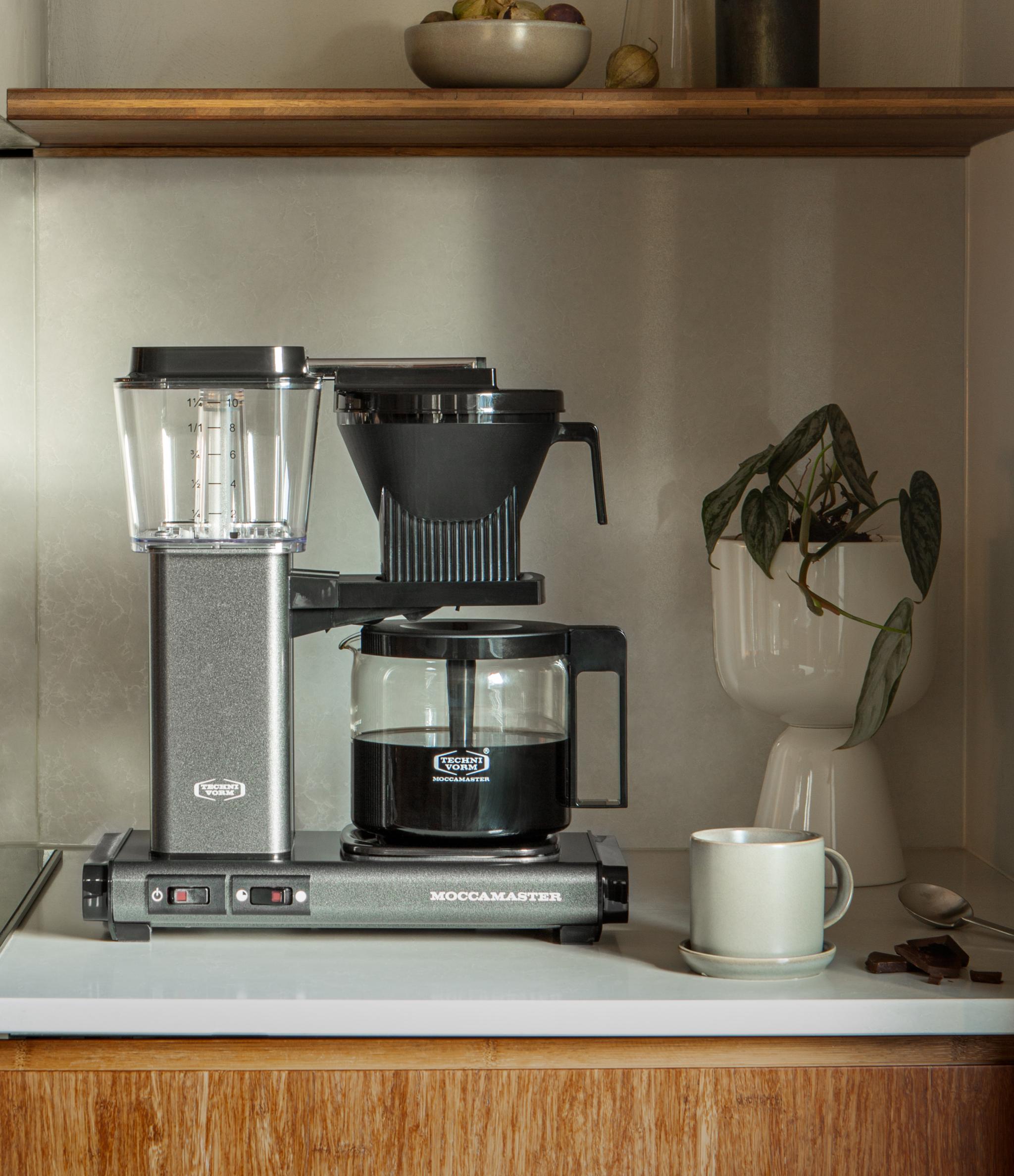 Stilren kjøkkenbenk med Moccamaster kaffetrakter, kaffekopp og grønne planter i et moderne, nordisk interiør.
