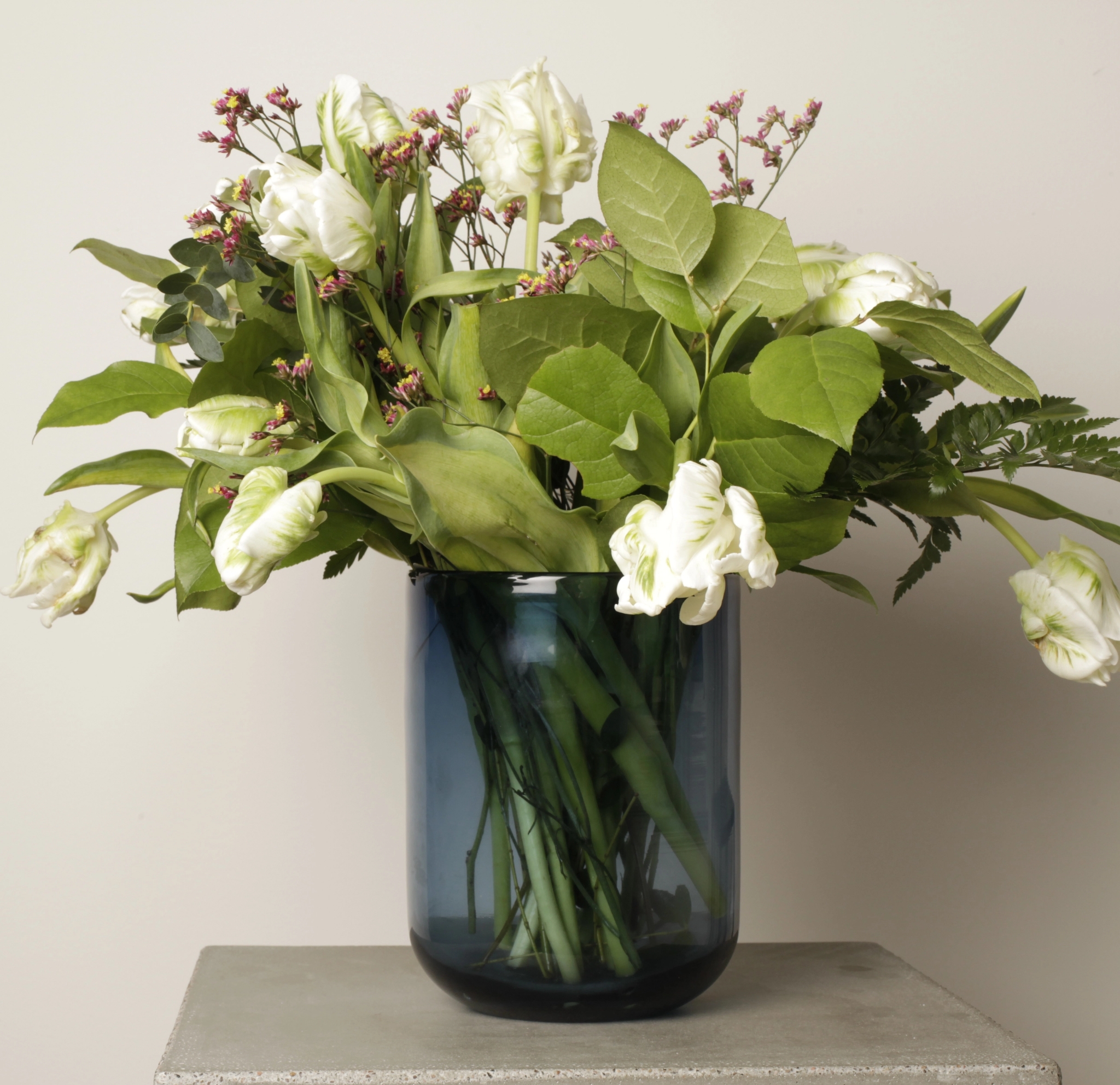 Sininen lasimaljakko ison kukkakimpun kera