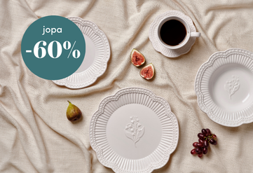 Tyylikkäästi katettu pöytä, jossa valkoiset koristeelliset lautaset, kahvikuppi ja hedelmiä, sekä vihreä ympyräteksti 'jopa -60 %' alennuksesta.
