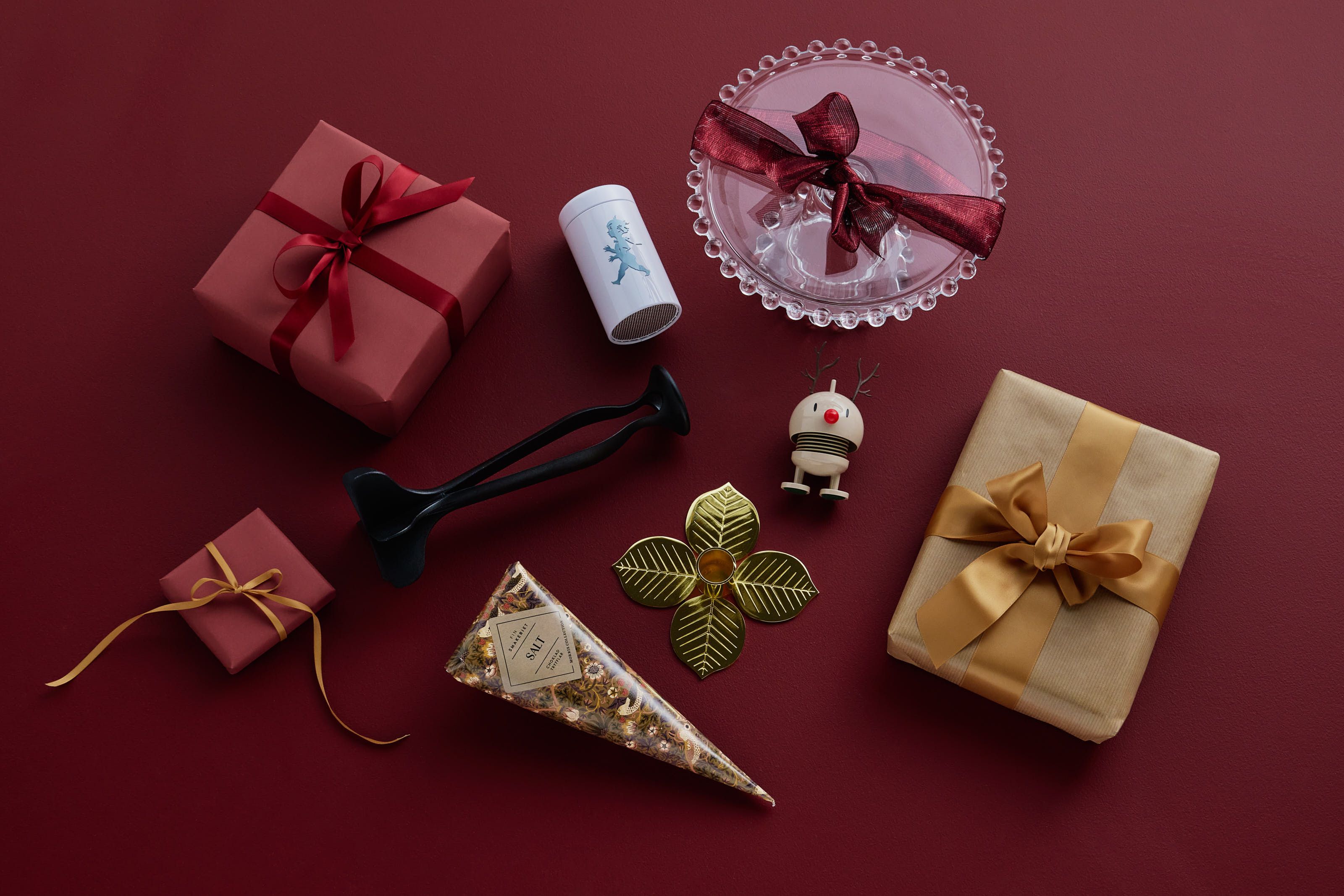 Julklappar till julklappsspelet ligger bland inslagna julklappar mot en röd bakgrund