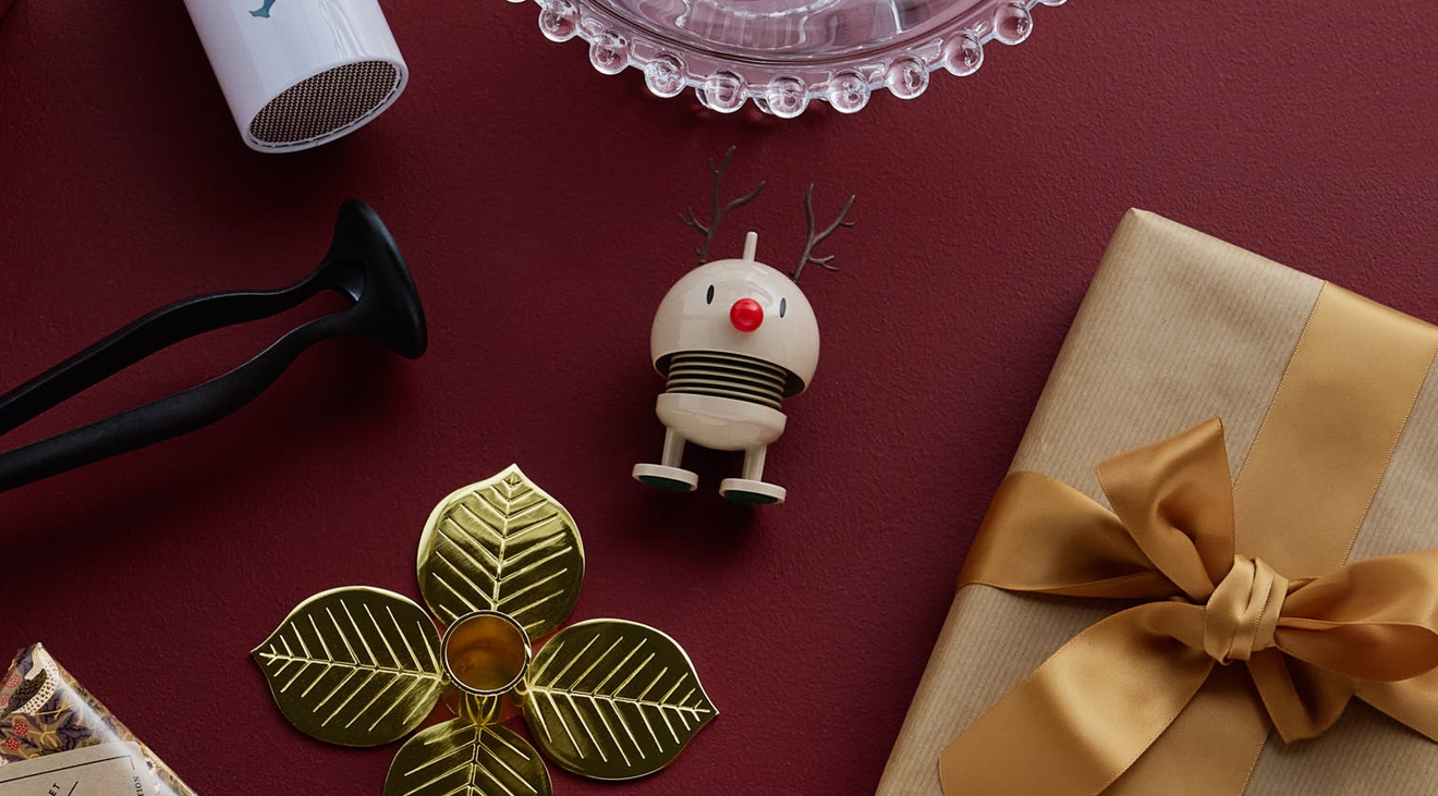 Ulike innpakkede gaver og små dekorative gjenstander arrangert på en dyp rød overflate
