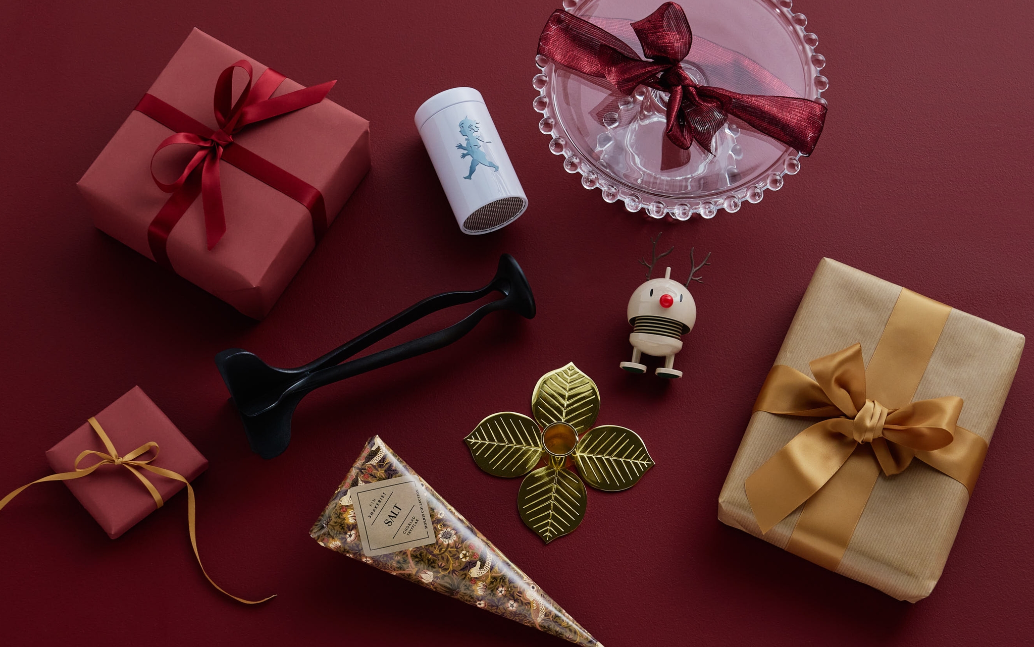 Kokoelma lahjapaketteja ja juhlavia koristeita punaisella taustalla.