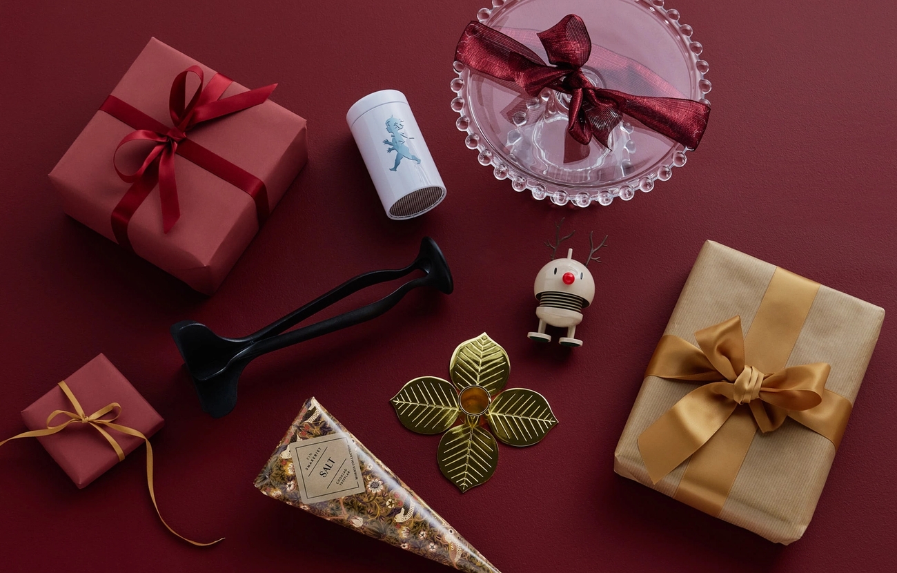 Julklappar till julklappsspelet ligger bland inslagna julklappar mot en röd bakgrund
