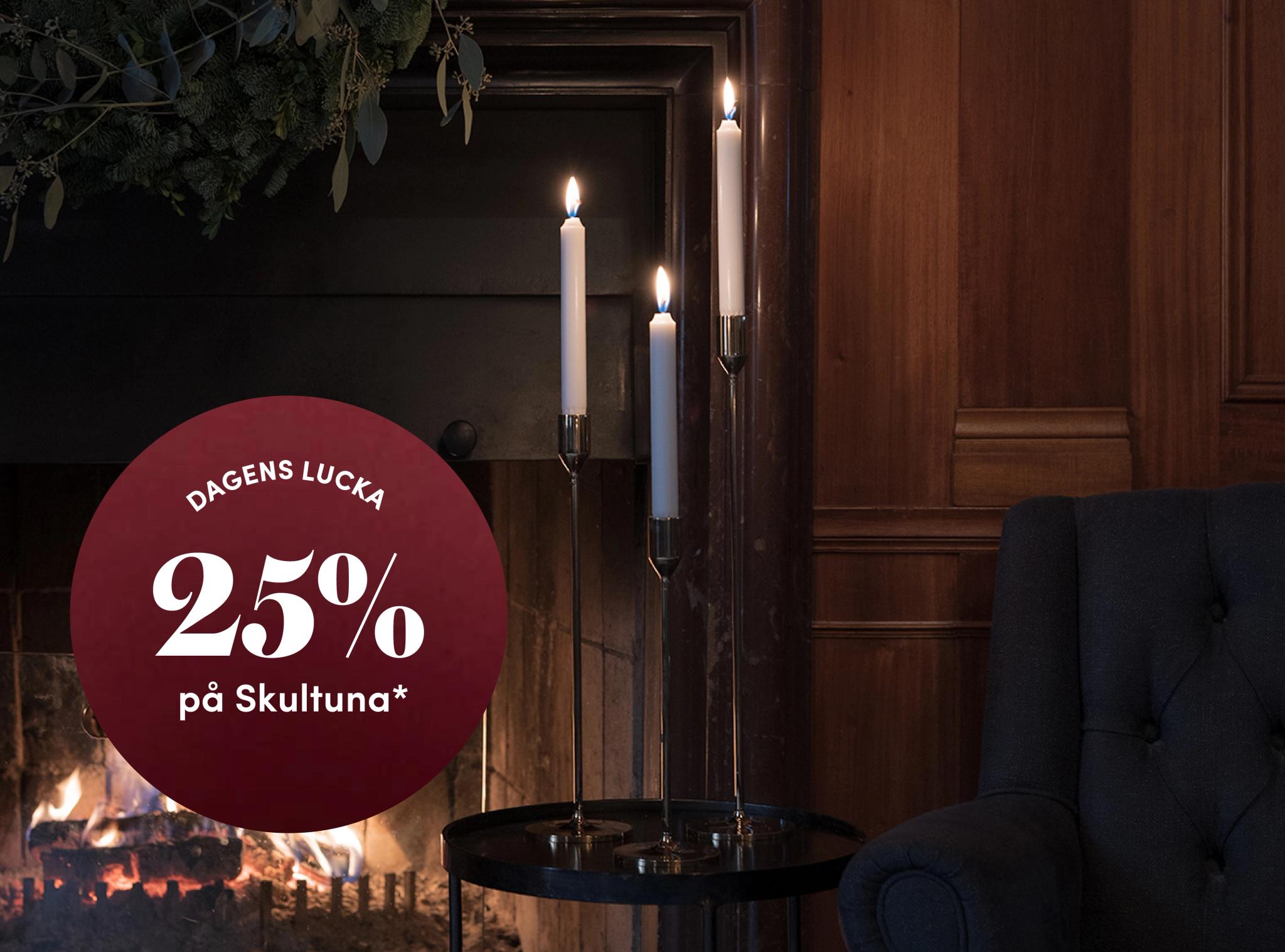 A warm room with a lit fireplace, three burning candles on a side table, and a red circular overlay announcing "Dagens Lucka 25% på Skultuna*".