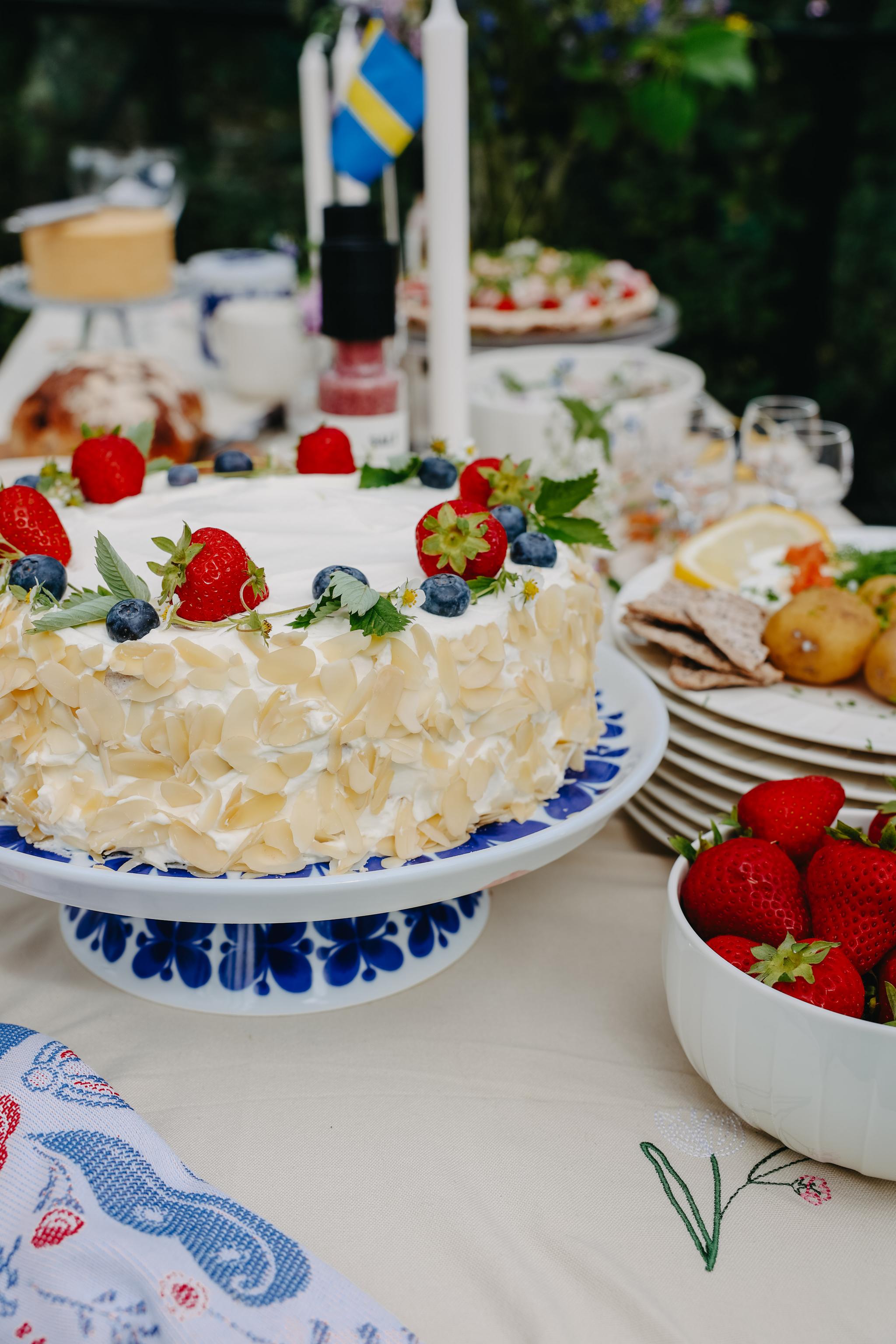 Somrig gräddtårta med jordgubbar och blåbär på ett dukat svenskt festbord.