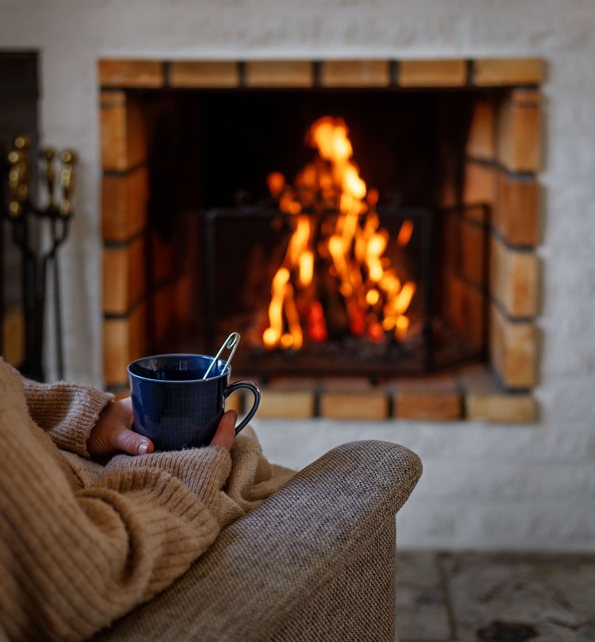 En person sitter i en fåtölj och dricker te framför en brasa