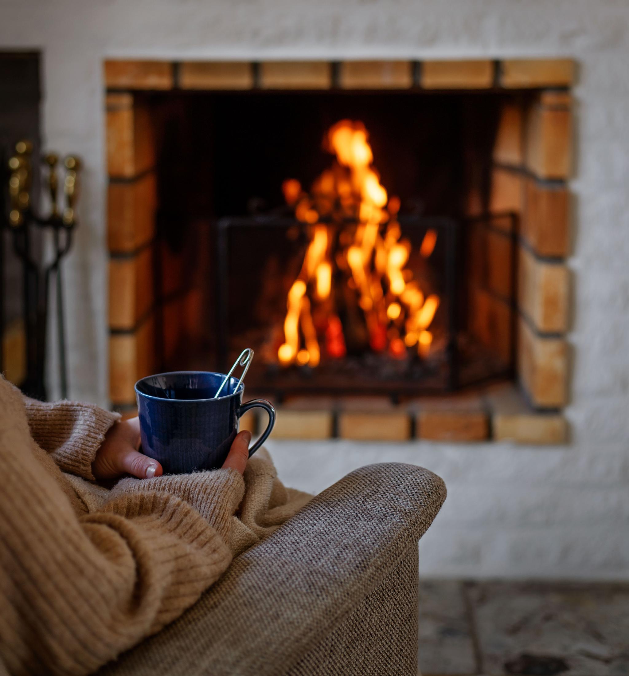 En person sitter i en fåtölj och dricker te framför en brasa