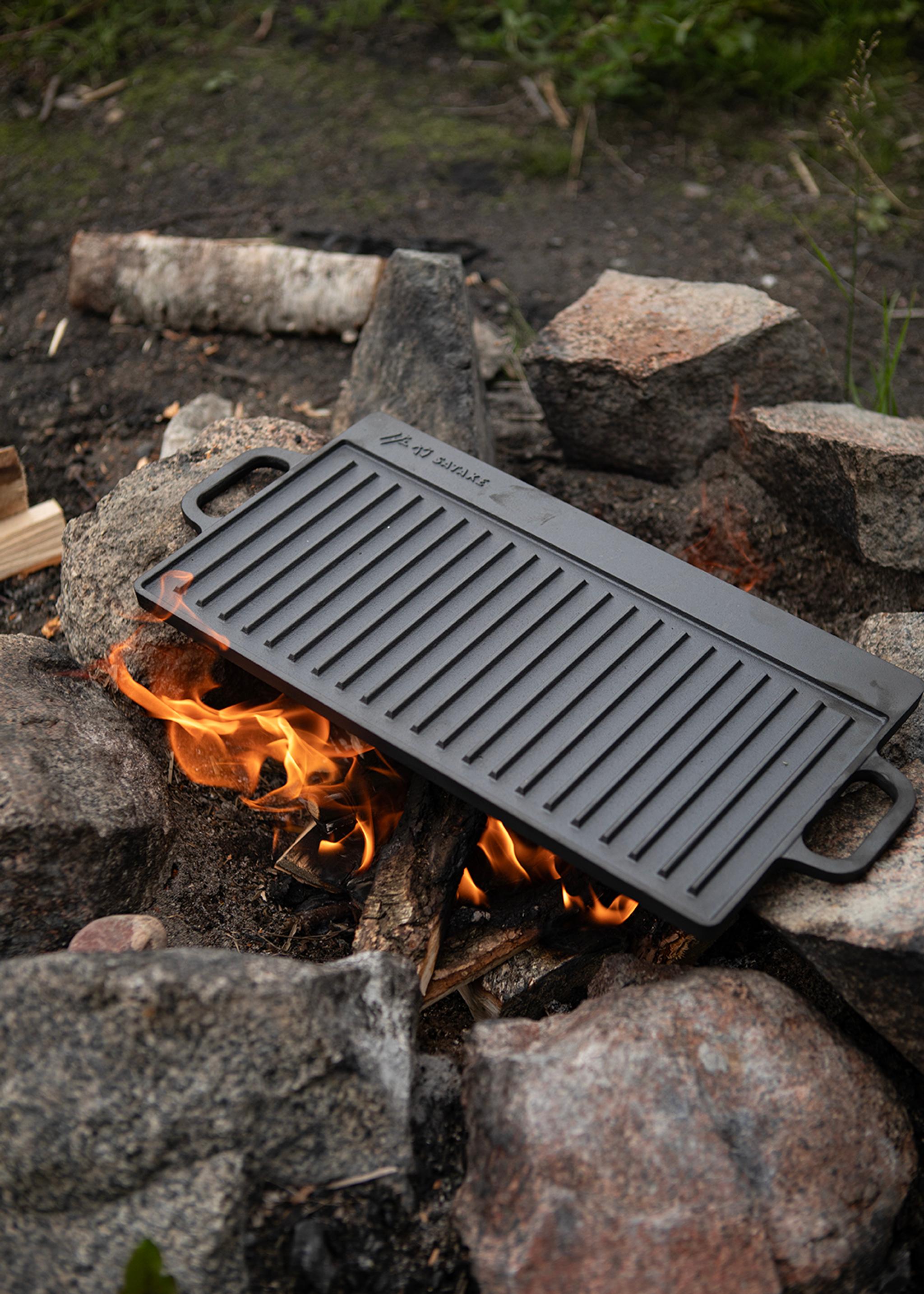 En gjutjärnsgrillplatta ligger över öppen eld på en stenring utomhus.