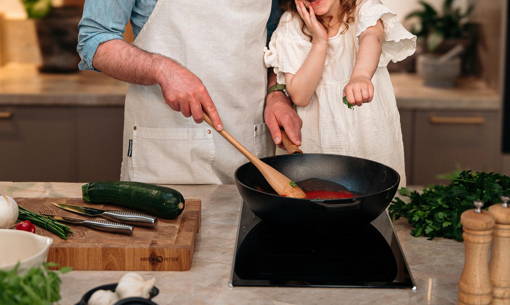 Leende pappa och dotter lagar mat tillsammans vid spisen i ett modernt kök, med Cervera-loggan ovanför.