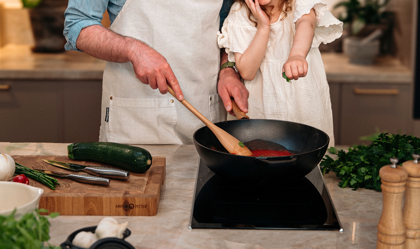 Leende pappa och dotter lagar mat tillsammans vid spisen i ett modernt kök, med Cervera-loggan ovanför.