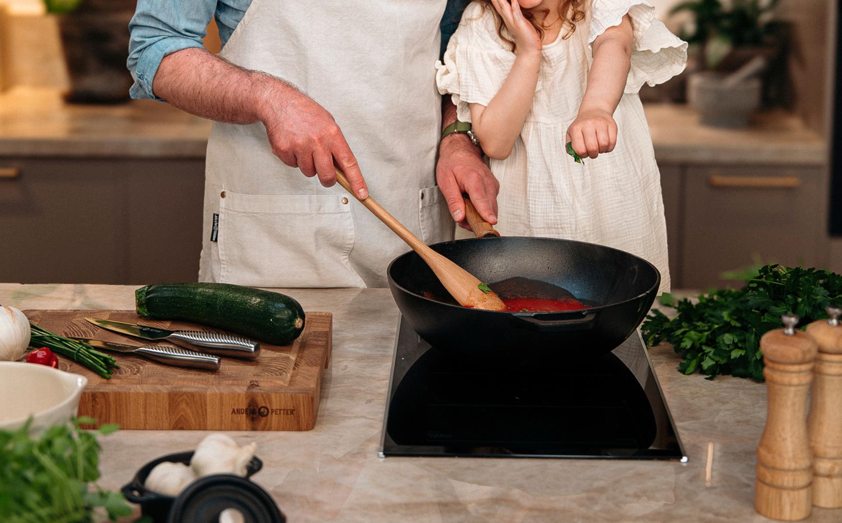Leende pappa och dotter lagar mat tillsammans vid spisen i ett modernt kök, med Cervera-loggan ovanför.