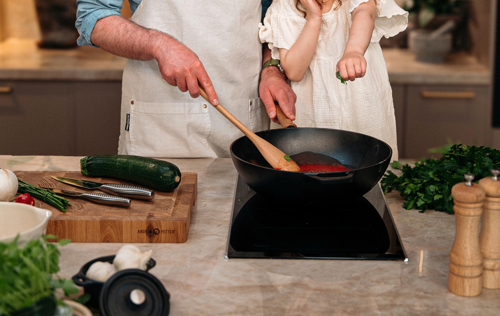 Leende pappa och dotter lagar mat tillsammans vid spisen i ett modernt kök, med Cervera-loggan ovanför.