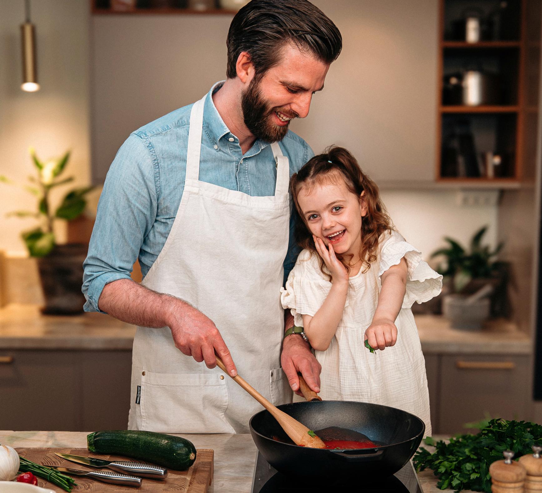 Leende pappa och dotter lagar mat tillsammans vid spisen i ett modernt kök, med Cervera-loggan ovanför.