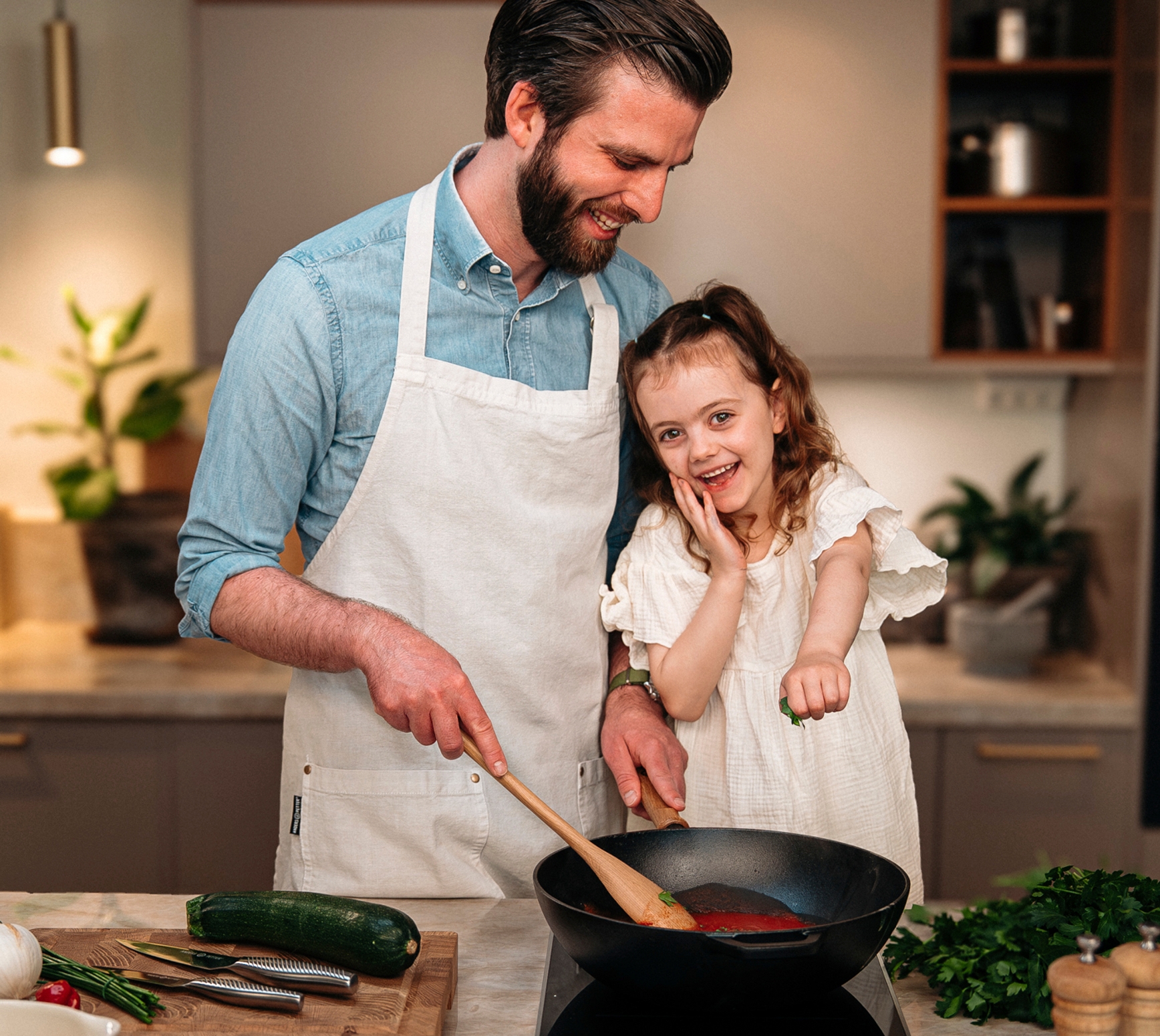 Pappa och dotter lagar mat tillsammans vid spisen i ett modernt kök med Cervera-produkter.