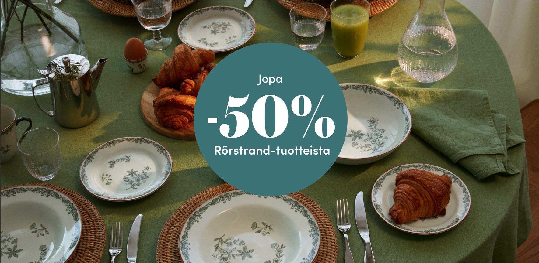 Vihreälle aamiaispöydälle katetut Rörstrand-astiat ja croissantit, jopa 50 % alennuksessa.