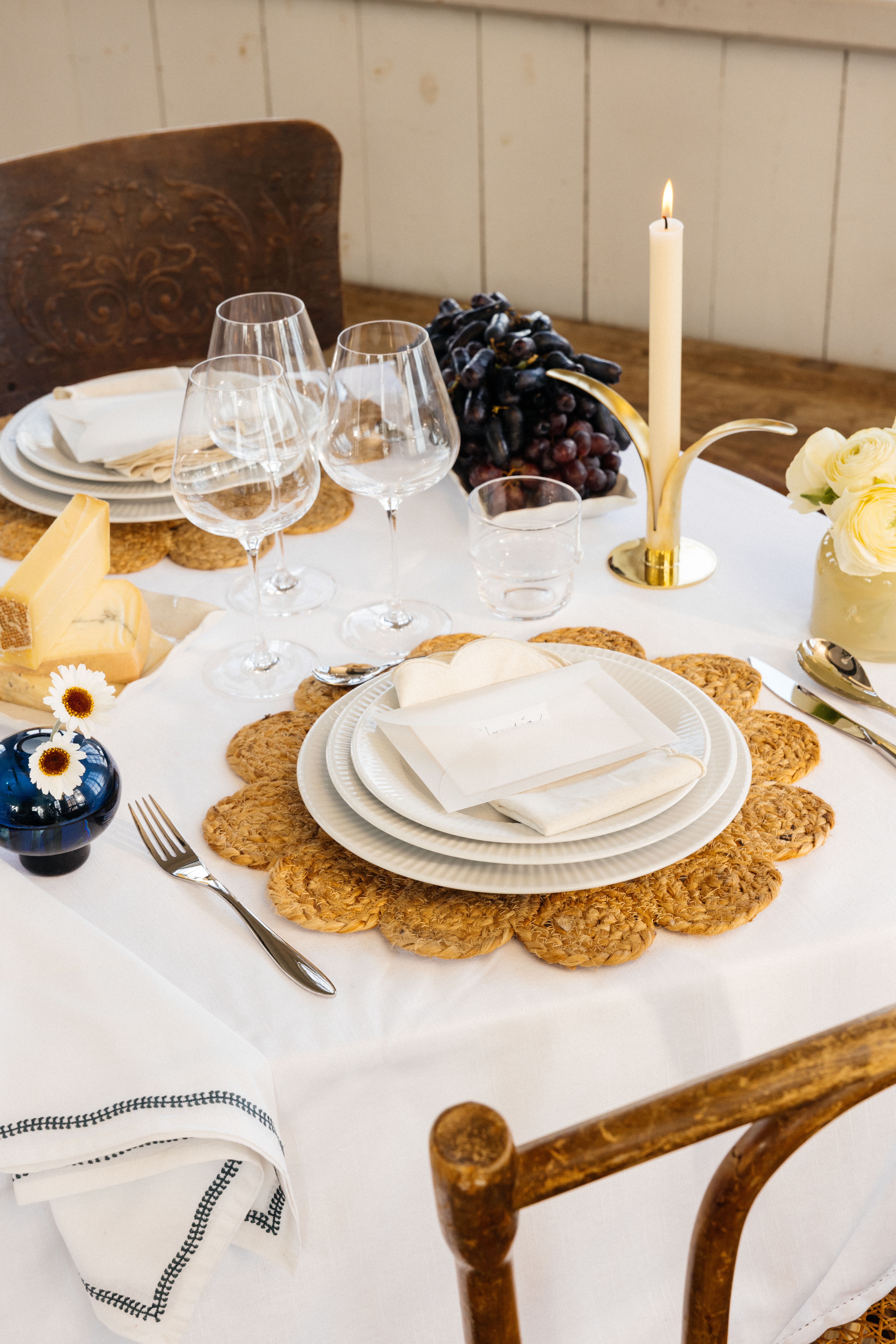 Festdukning med vit duk, bordstabletter, vitt porslin samt gula och blå vaser med blommor i