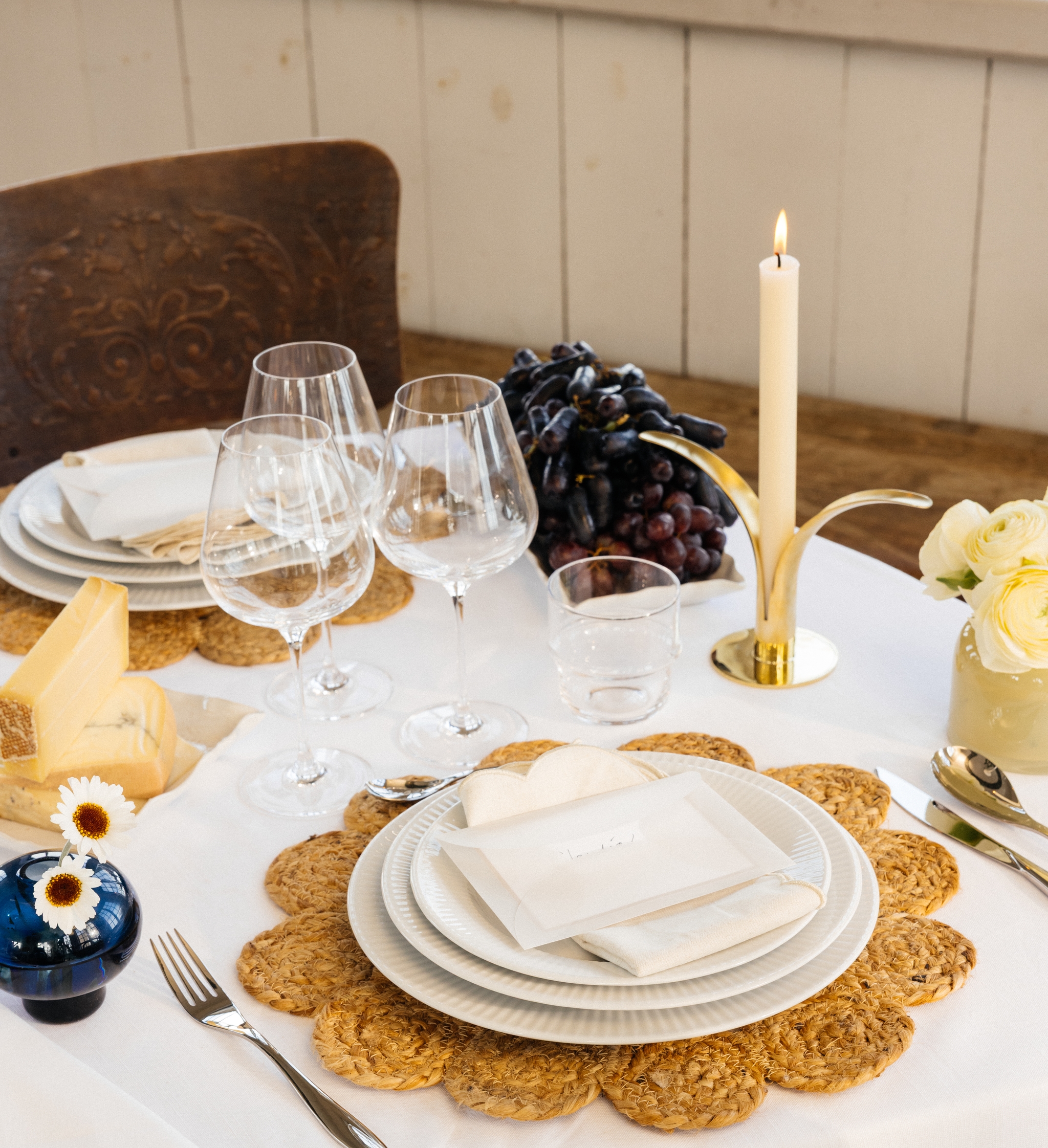 Festlig borddekking med hvit duk, dekkebrikker, hvitt porselen og gule og blå vaser med blomster i